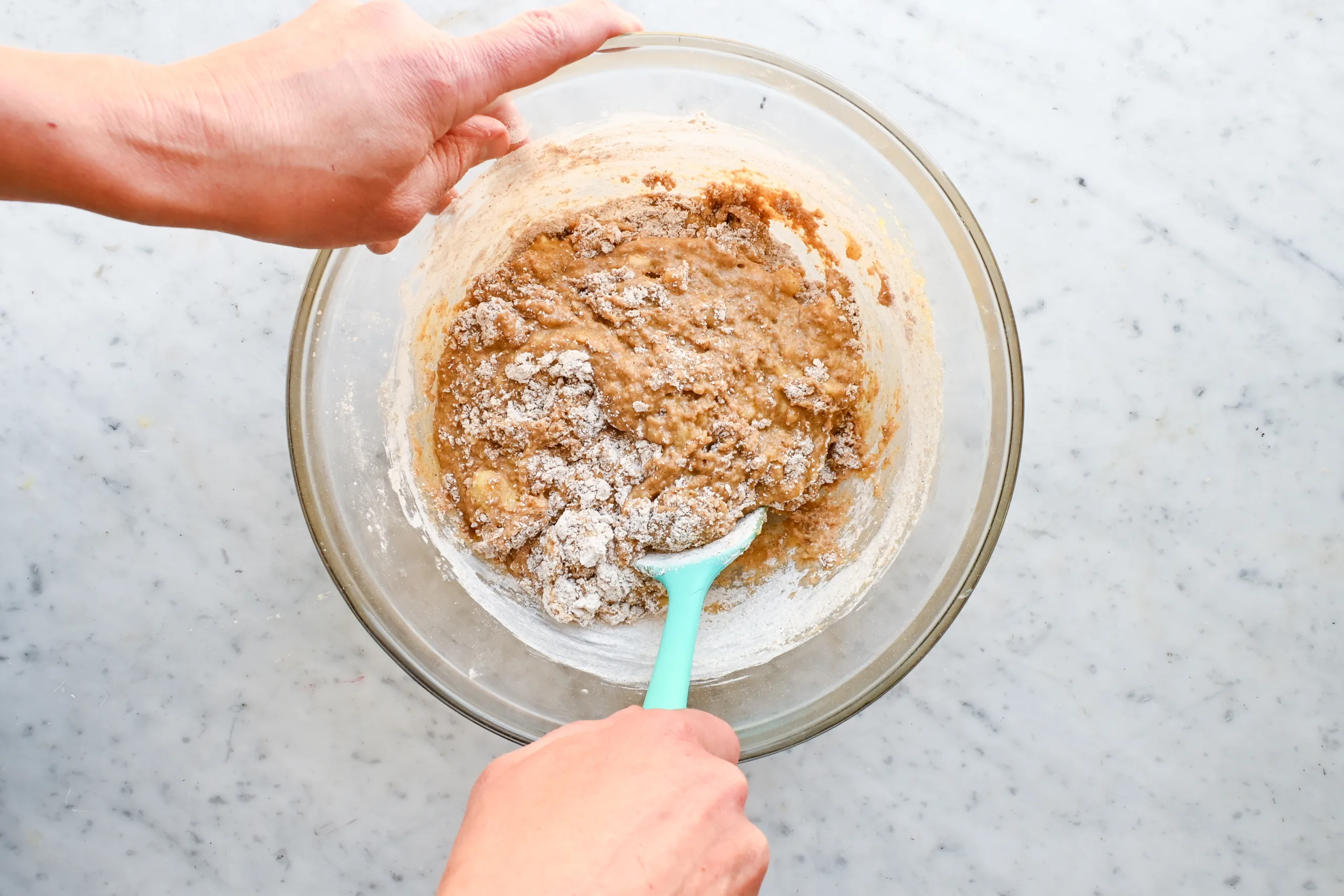Whole wheat banana muffin batter being gently mixed with a spatula.