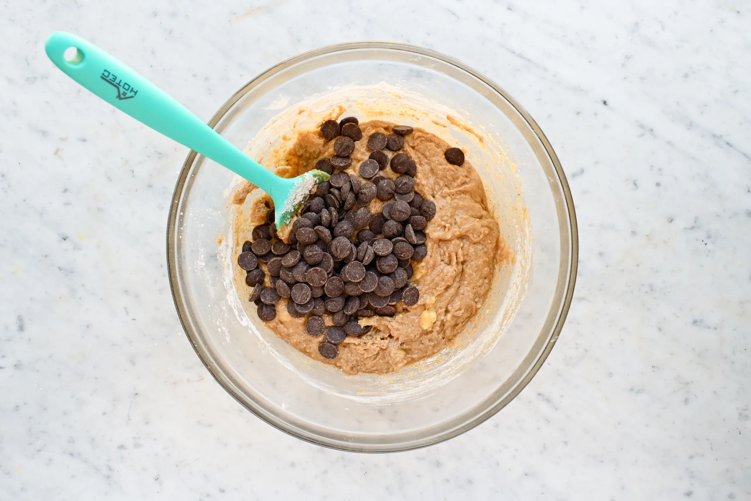 Chocolate chips added to whole wheat banana muffin batter in a glass bowl.