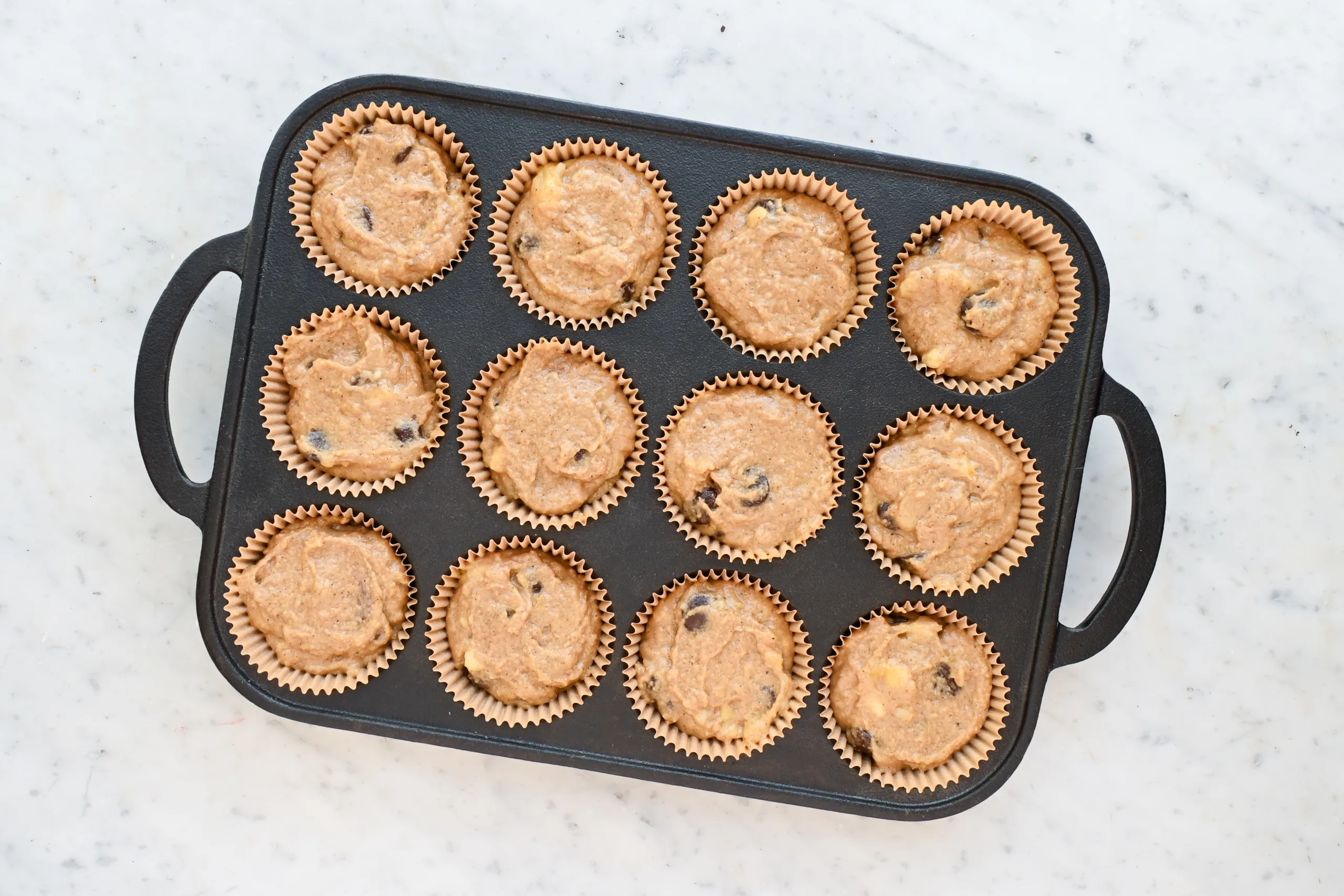 Whole wheat banana muffin batter divided into paper liners in a muffin tin before baking.