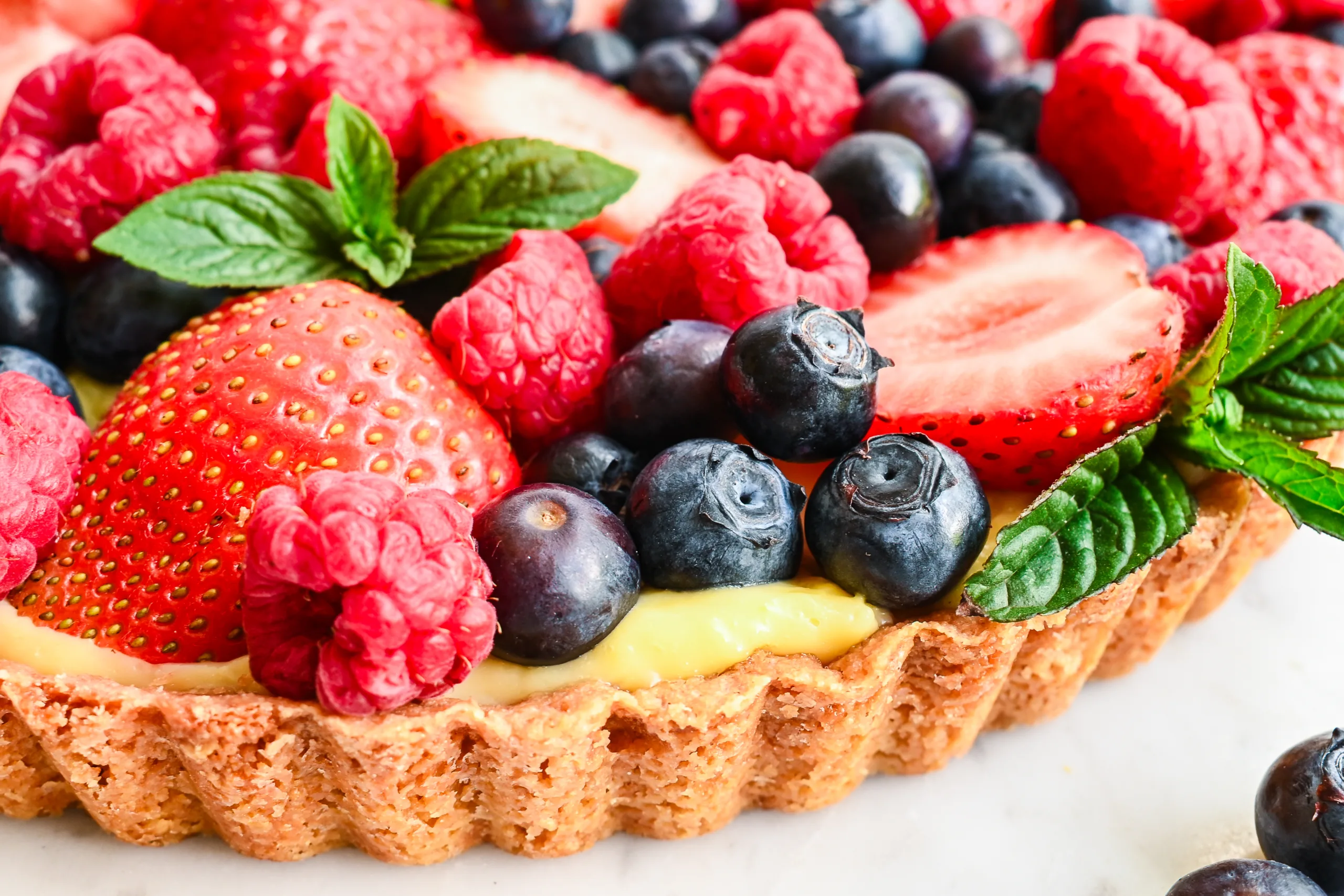 Close-up of a fresh berry cream tart with vanilla filling, strawberries, blueberries, raspberries, and mint.