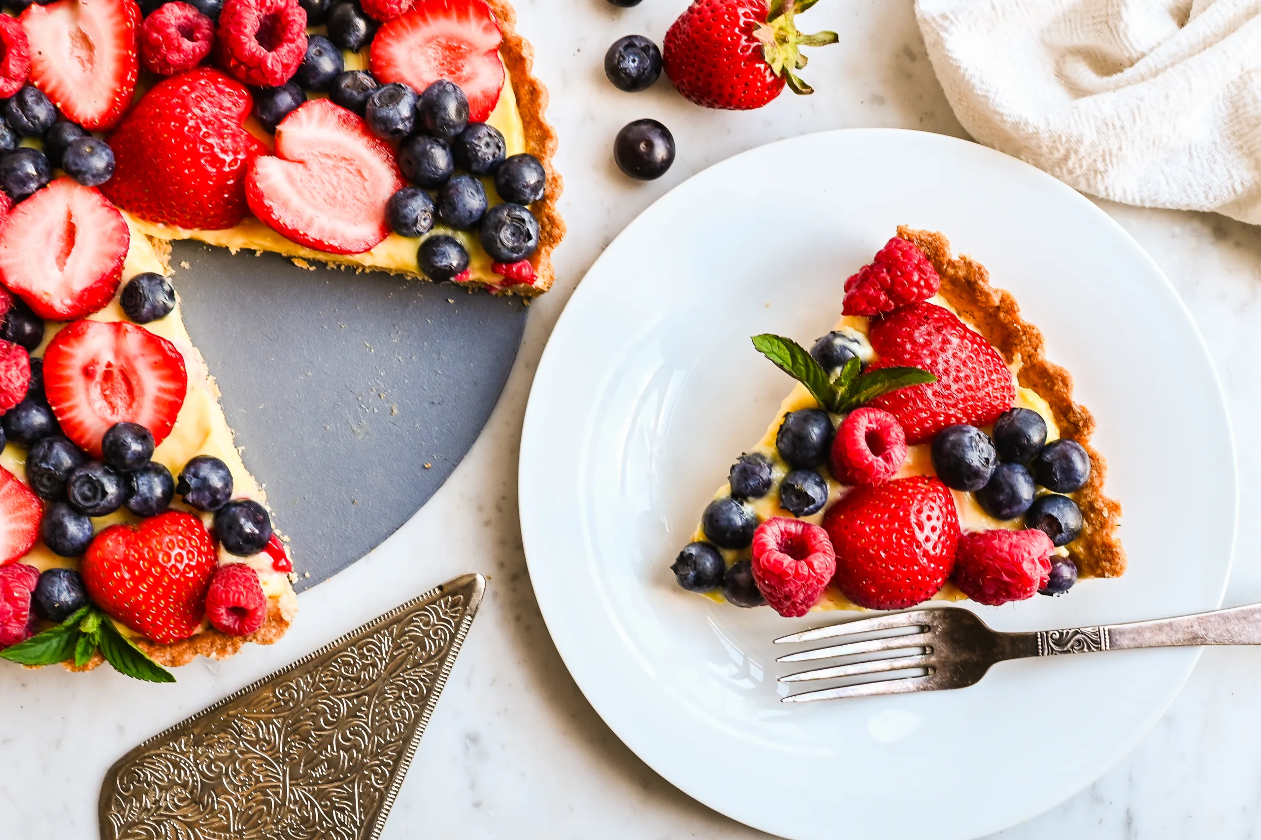 Overhead view of a fresh berry cream tart served with a plate and fork.