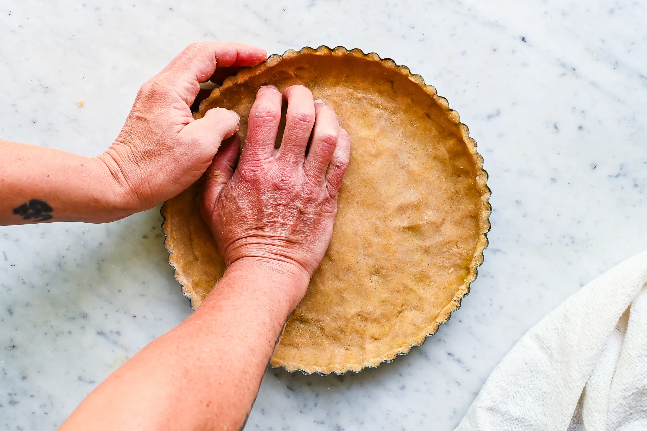 Homemade tart crust being pressed into a fluted tart pan.