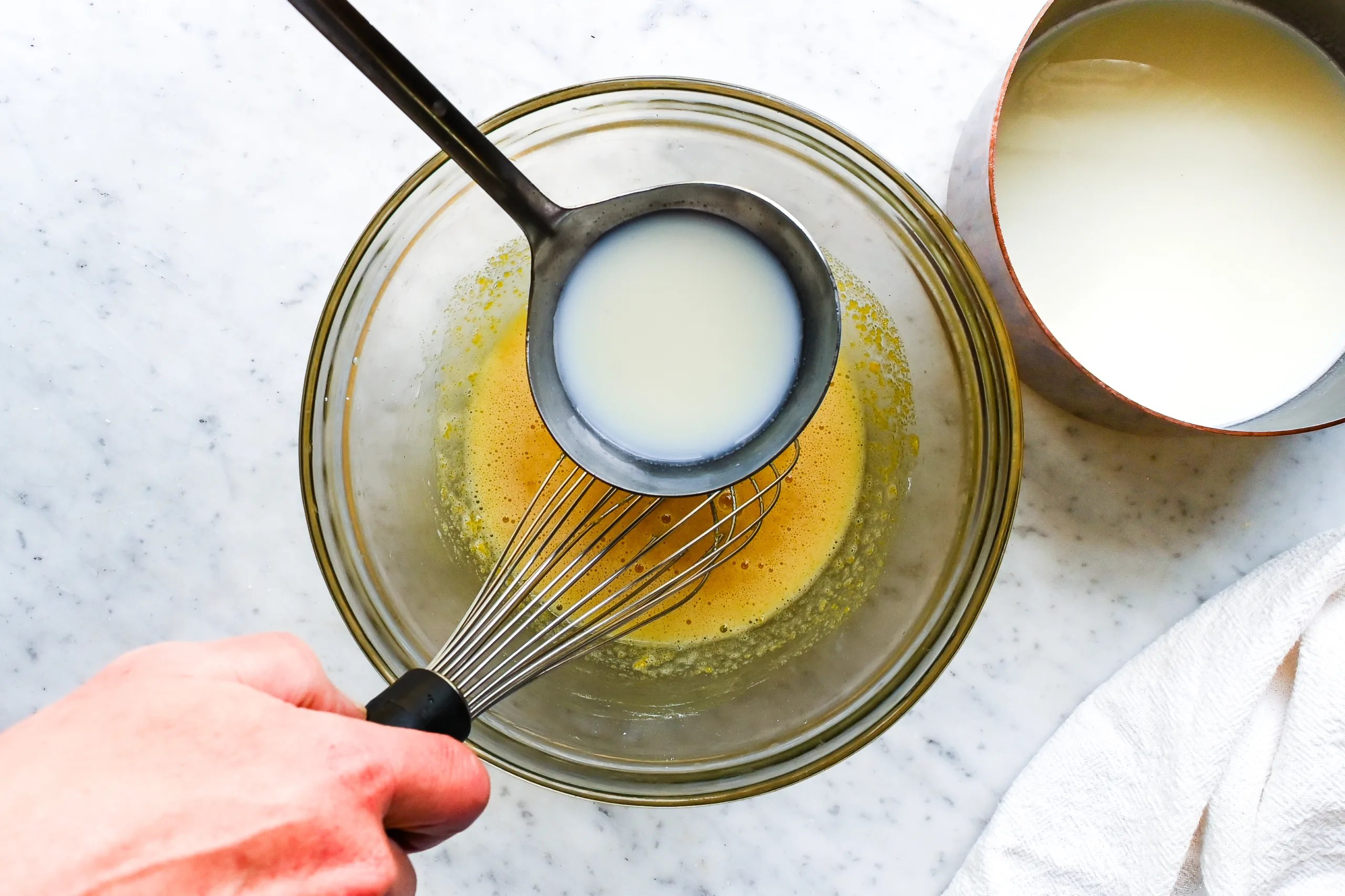 Warm milk being added to egg yolk mixture for homemade vanilla cream filling.