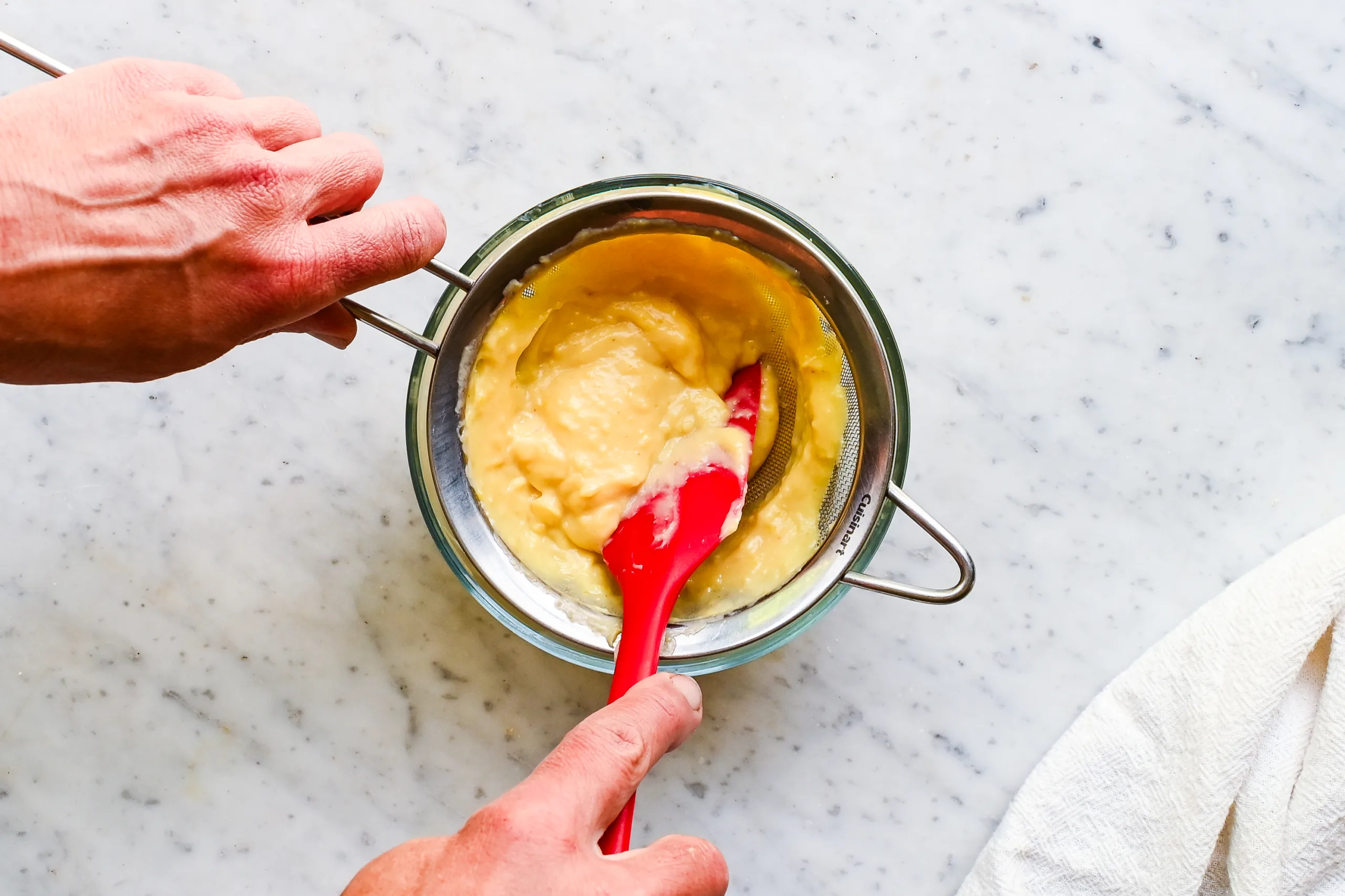Thick vanilla pastry cream being pressed through a fine mesh strainer for a smooth cream tart filling.