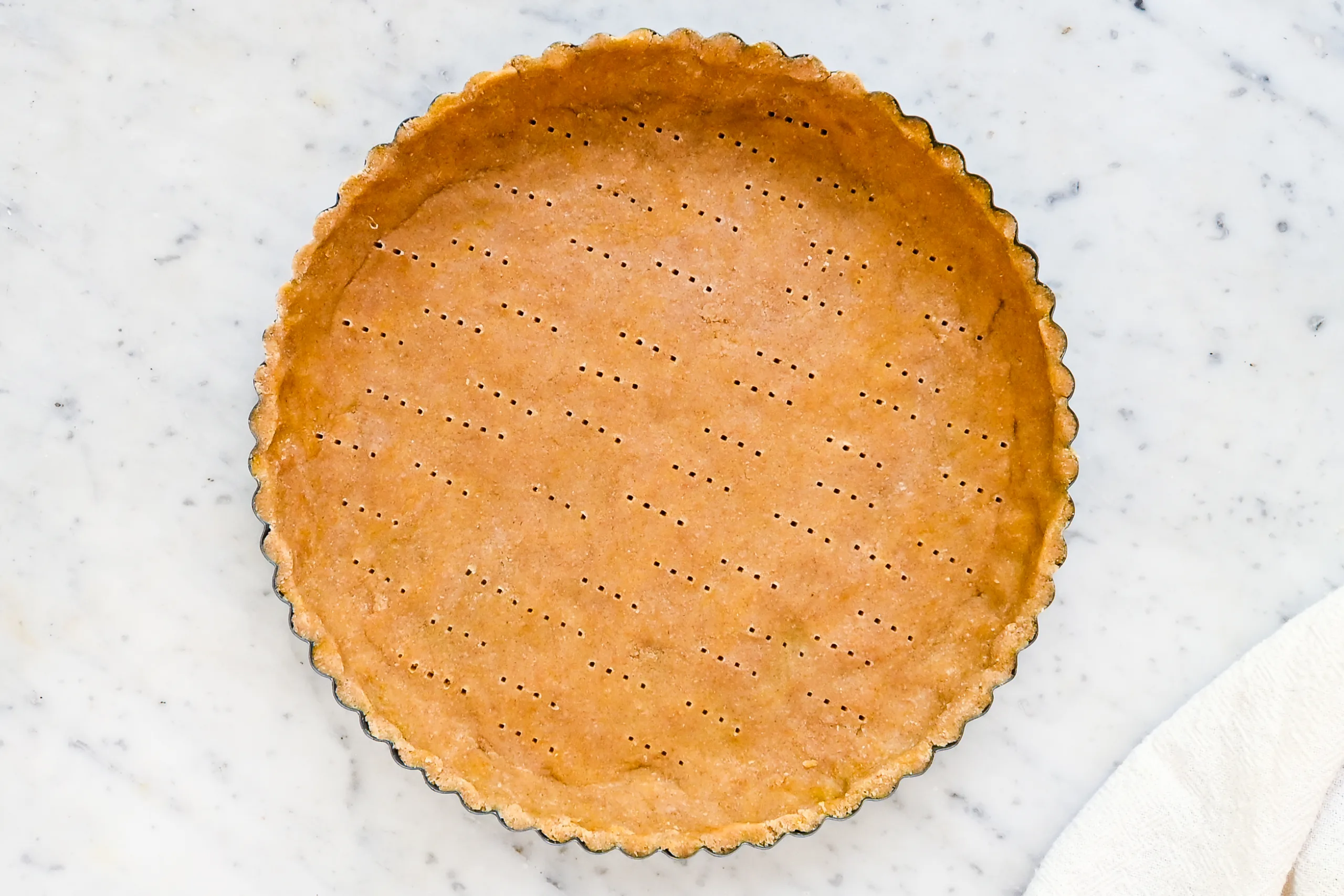 Unbaked tart crust pressed into a fluted tart pan and docked with fork holes before baking.