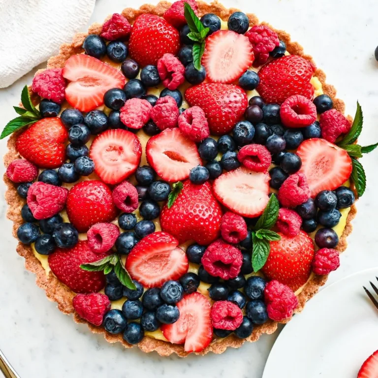 Fresh berry cream tart with vanilla cream filling, strawberries, blueberries, raspberries, and mint in a golden tart crust.