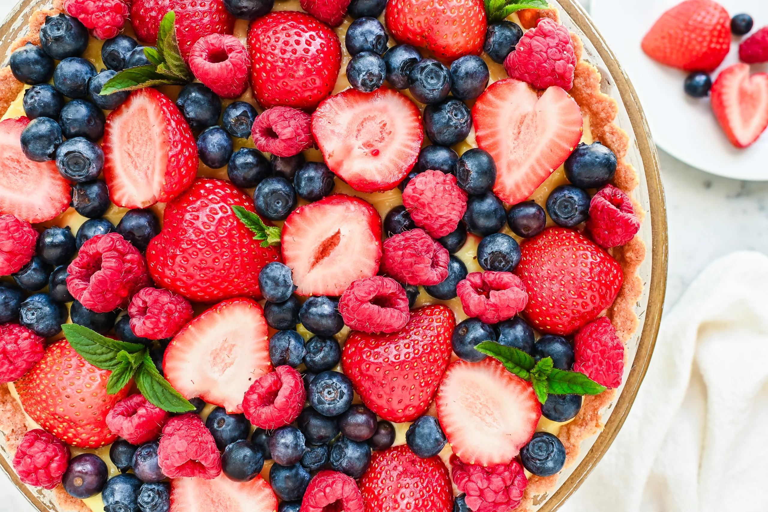 Close-up side view of a cream tart topped with fresh berries and mint.