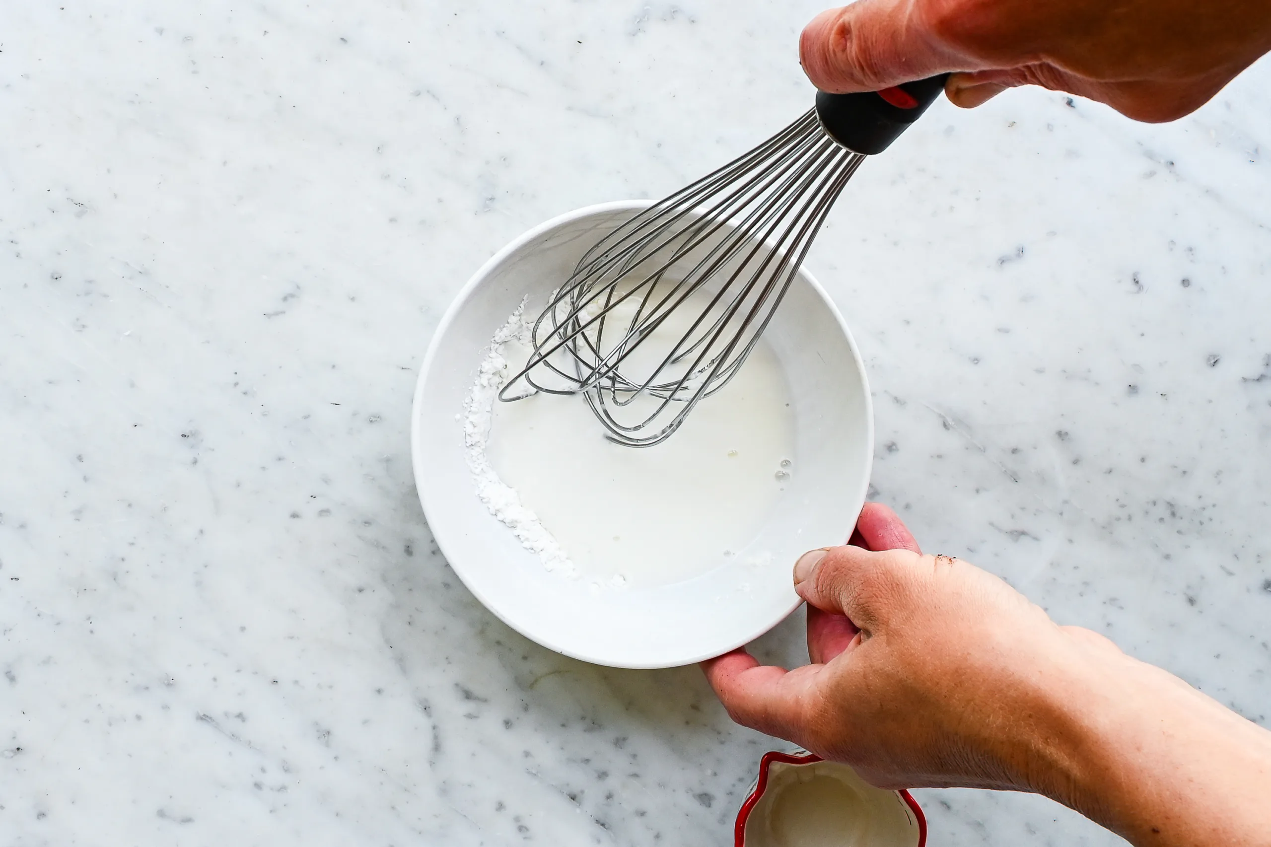 Cornstarch slurry being whisked in a white bowl for thickening apple pie filling.