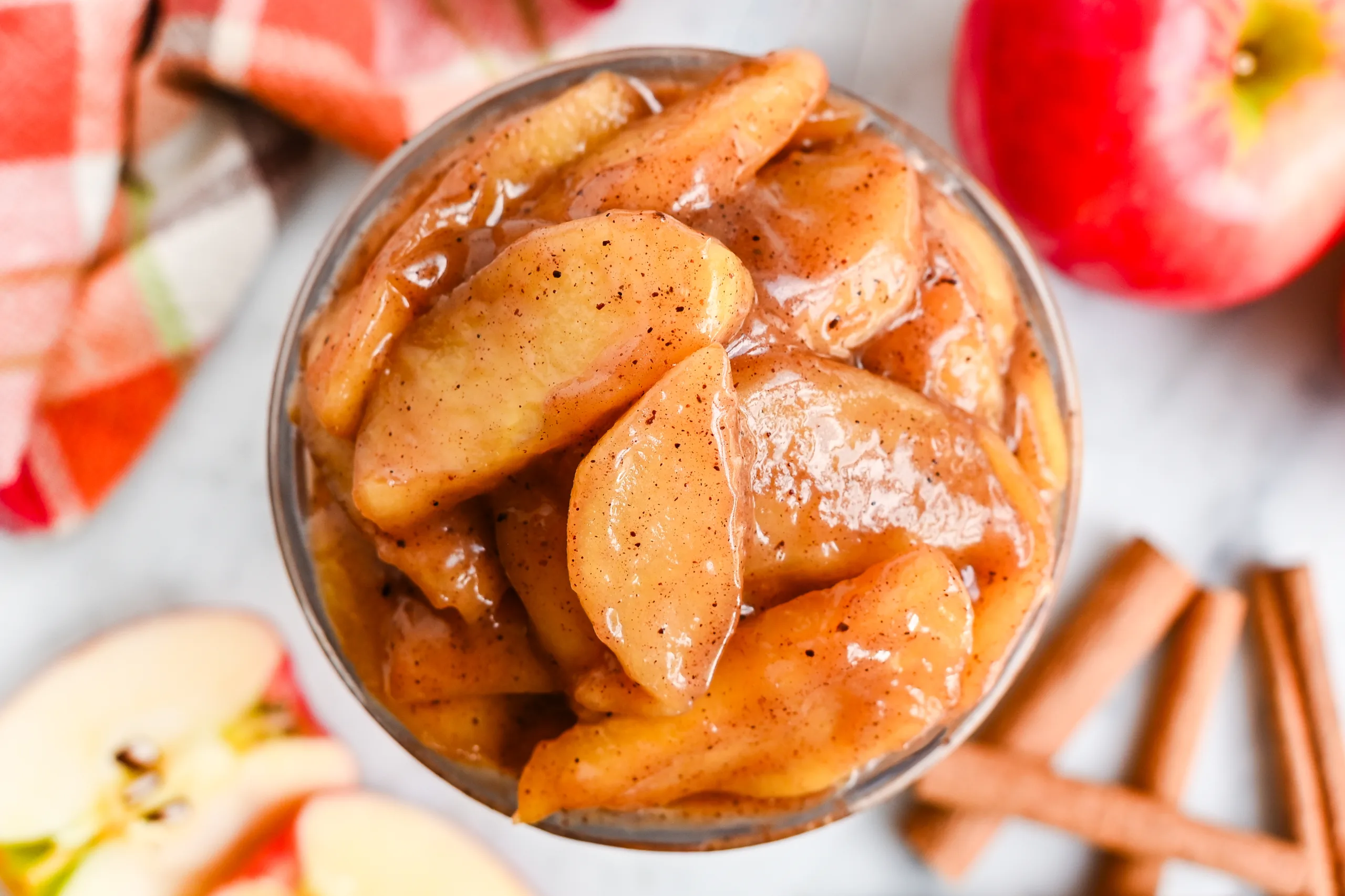 Homemade apple pie filling in a glass jar with cinnamon sticks and fresh apples.