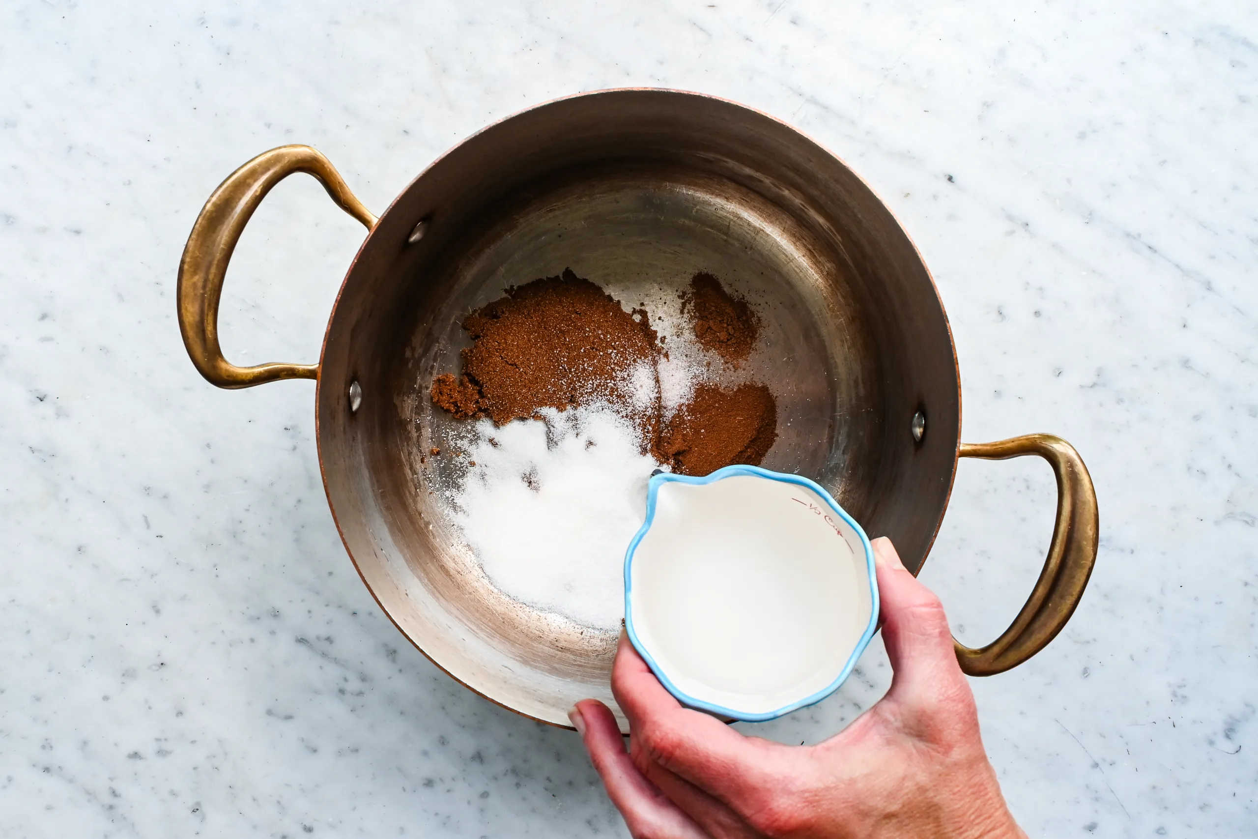 Water being added to brown sugar, granulated sugar, and spices in a copper pot.