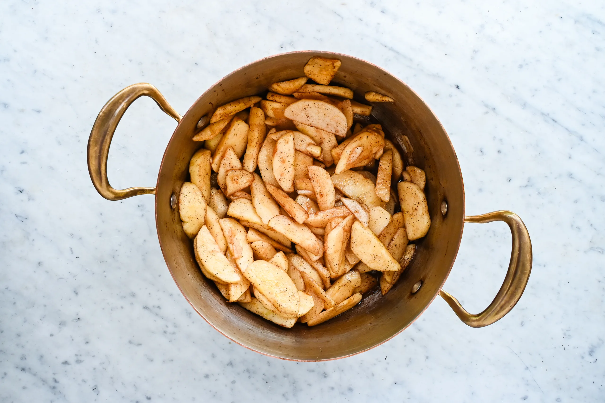 Sliced apples tossed with cinnamon and sugar in a copper pot.