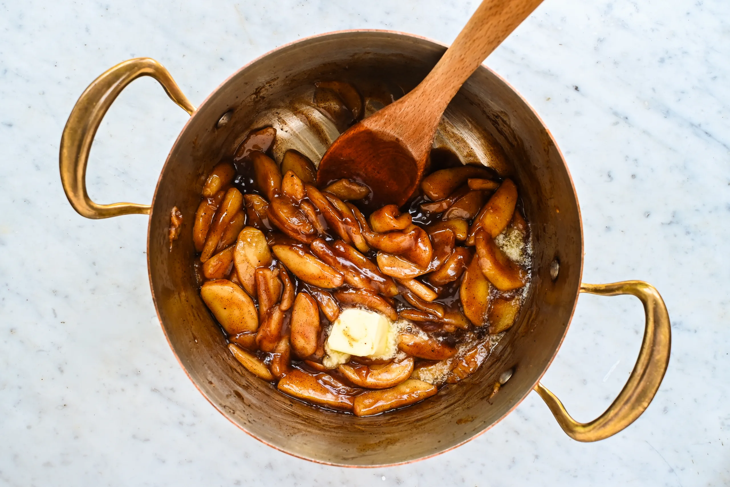 Butter added to cooked apple pie filling in a copper pot.