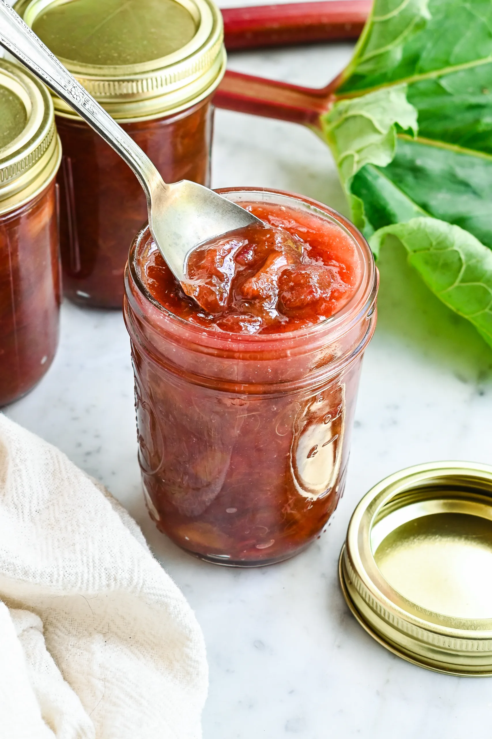 Close-up of chunky homemade rhubarb jam on a spoon above an open jar.