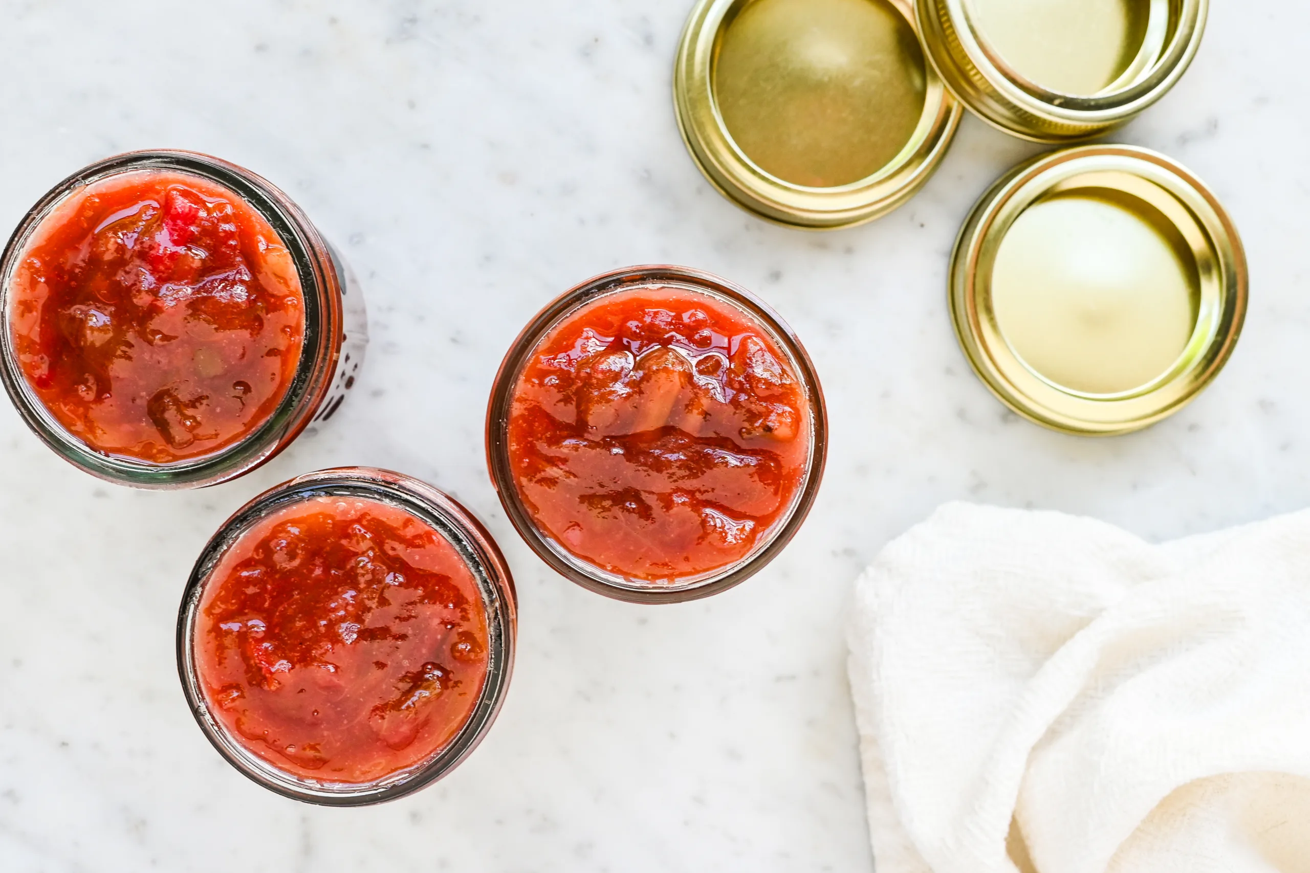 Three open jars filled with chunky homemade rhubarb jam on a marble counter.