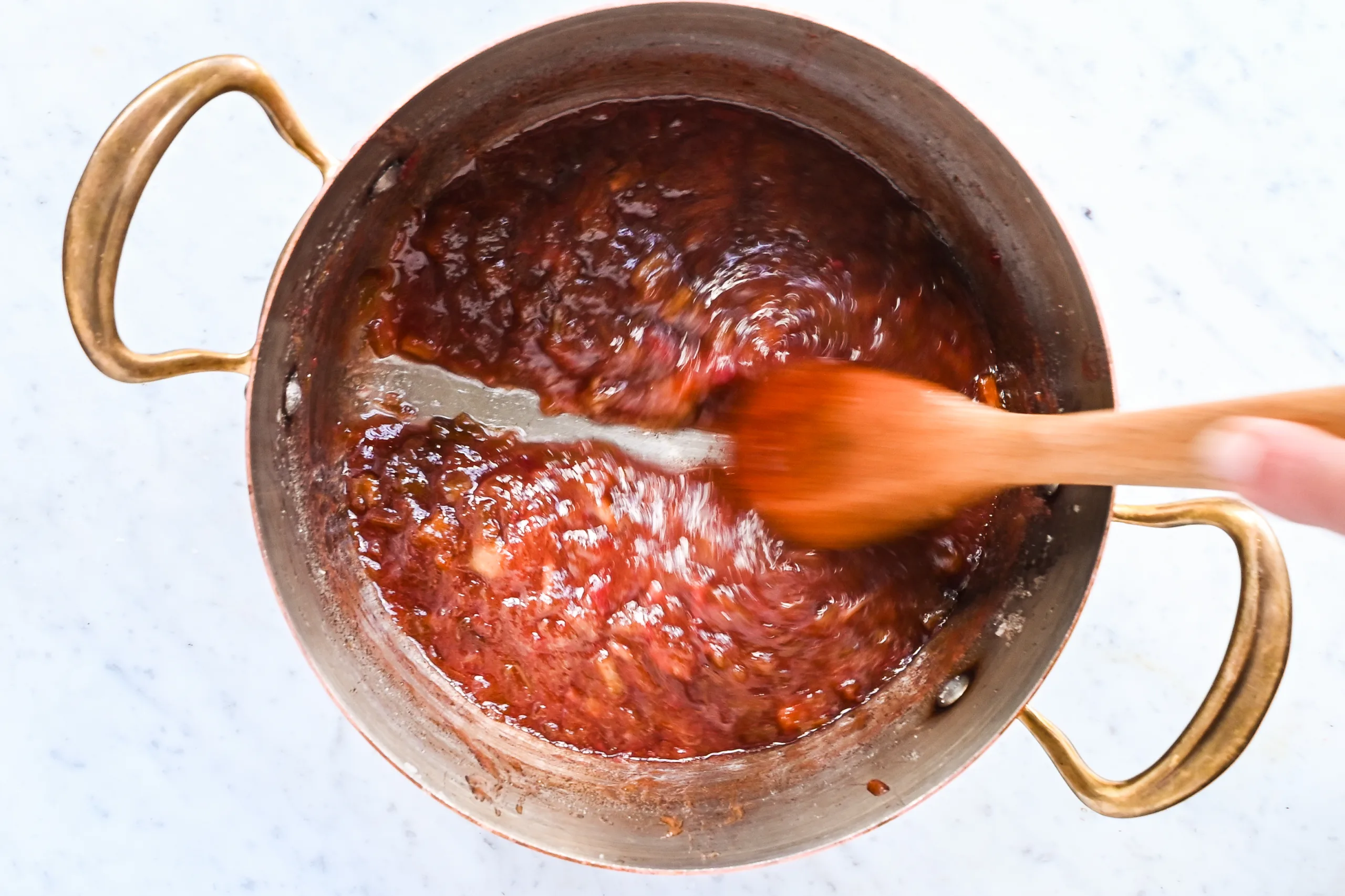 Thick rhubarb jam stirred with a wooden spoon as it cooks down.