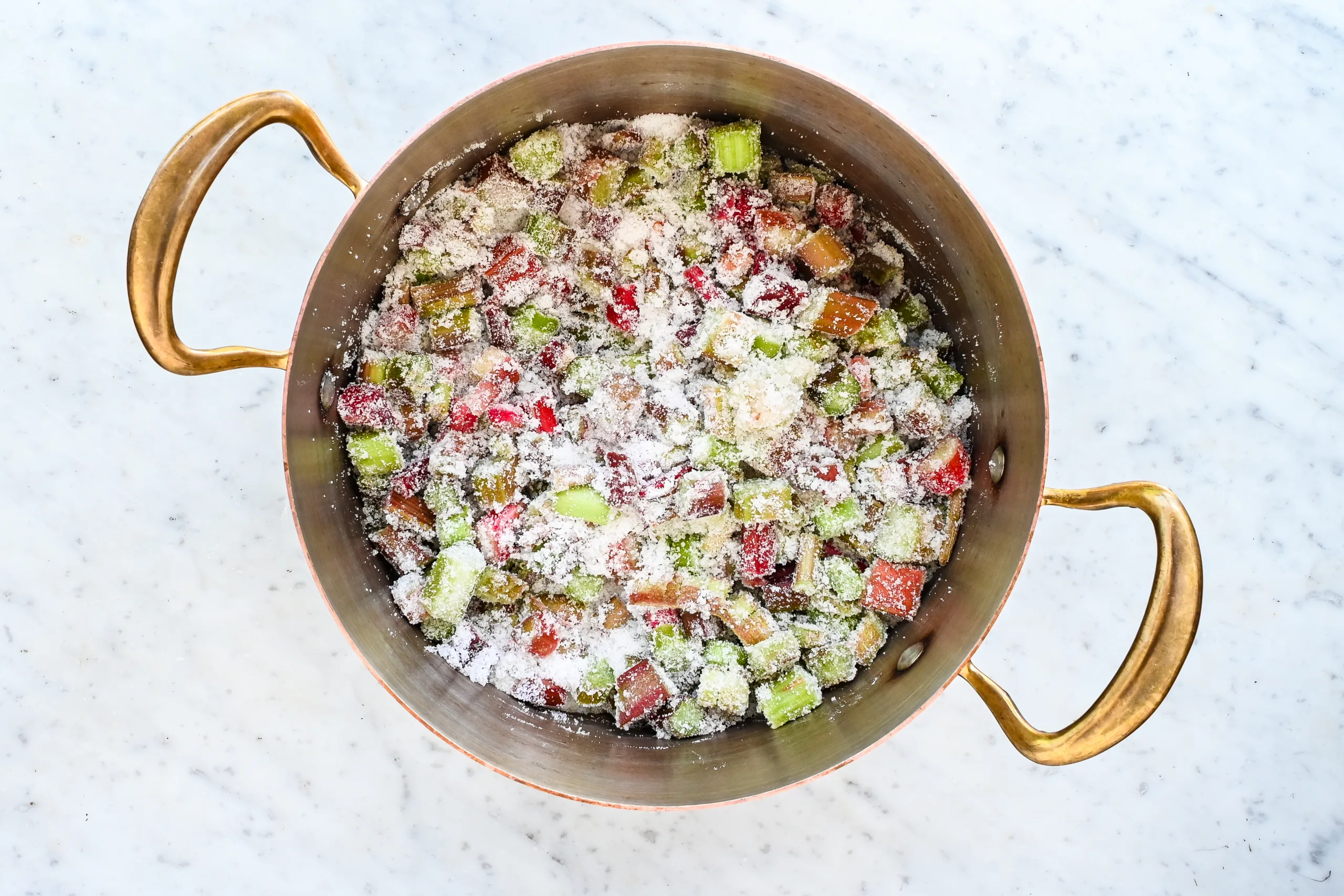 Chopped rhubarb mixed with sugar in a copper pot before cooking.