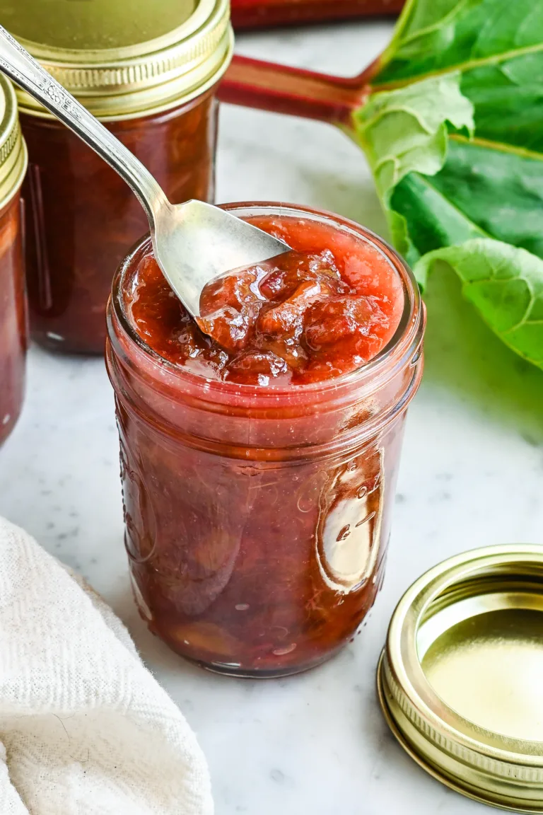 Thick homemade rhubarb jam scooped with a spoon from an open glass jar.