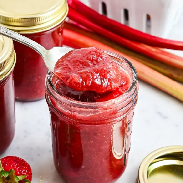 Homemade strawberry rhubarb jam spooned from a glass jar with fresh strawberries in the background.