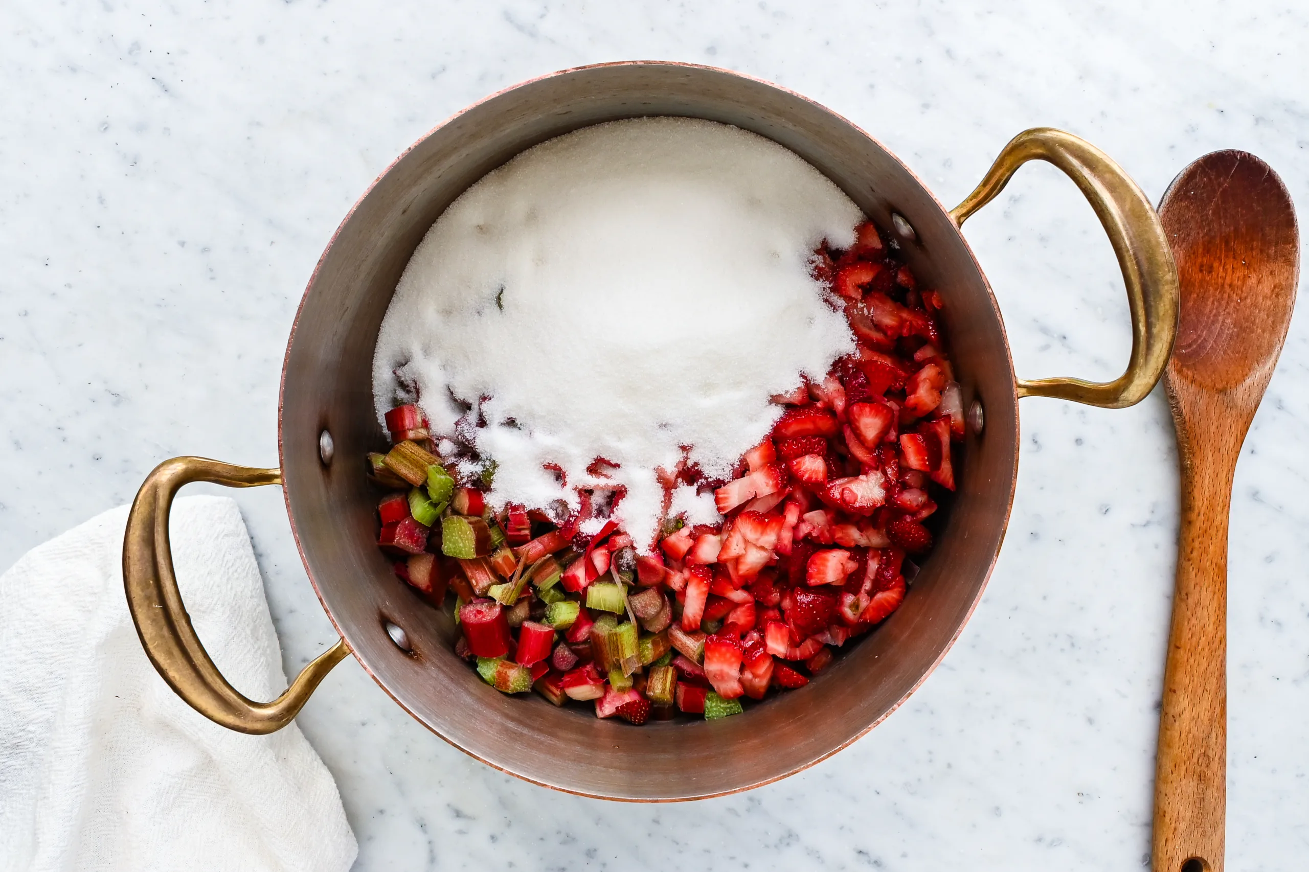 Chopped strawberries and rhubarb topped with granulated sugar in a large pot.