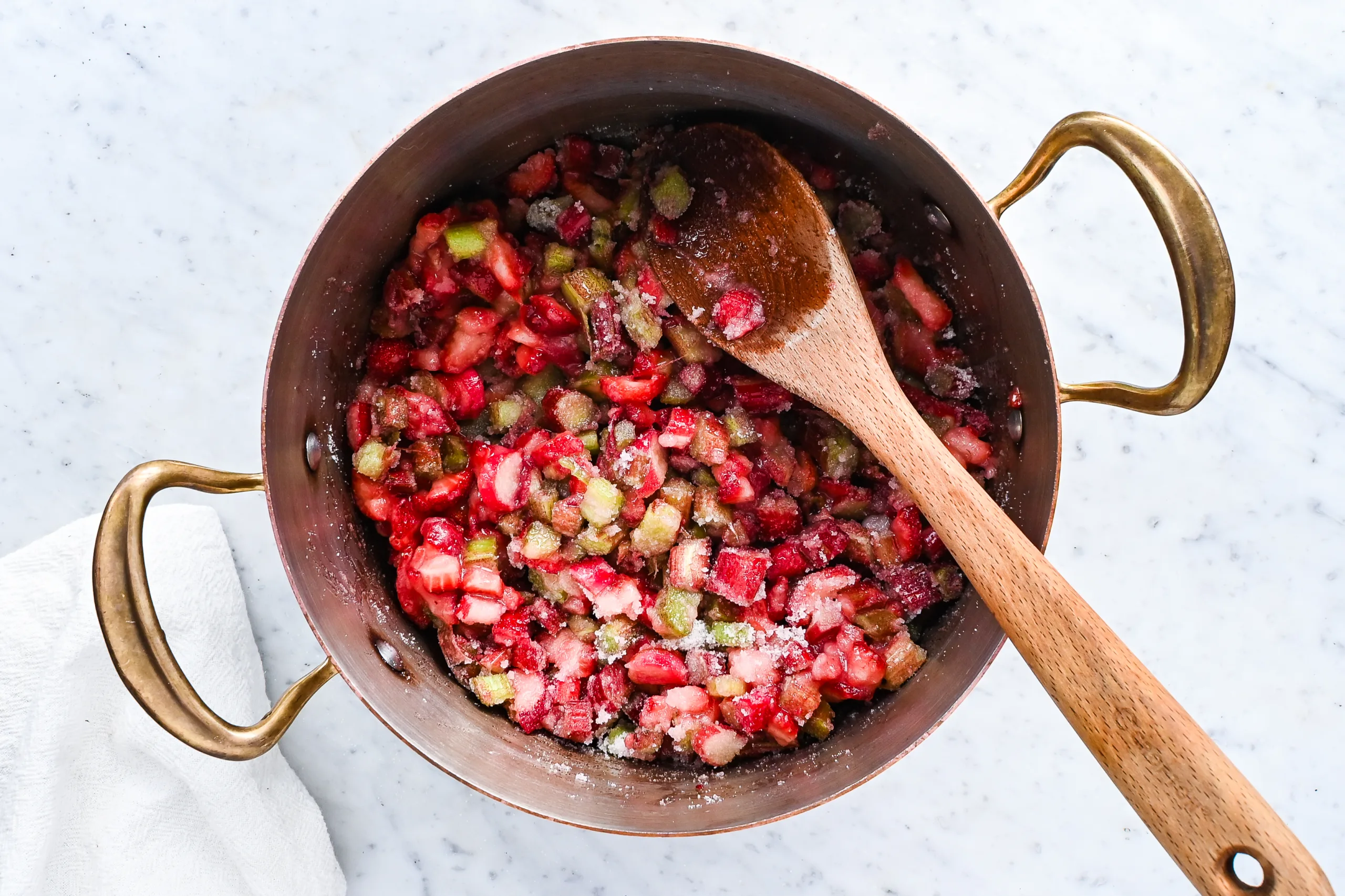 Strawberries, rhubarb, and sugar being stirred together before cooking the jam.