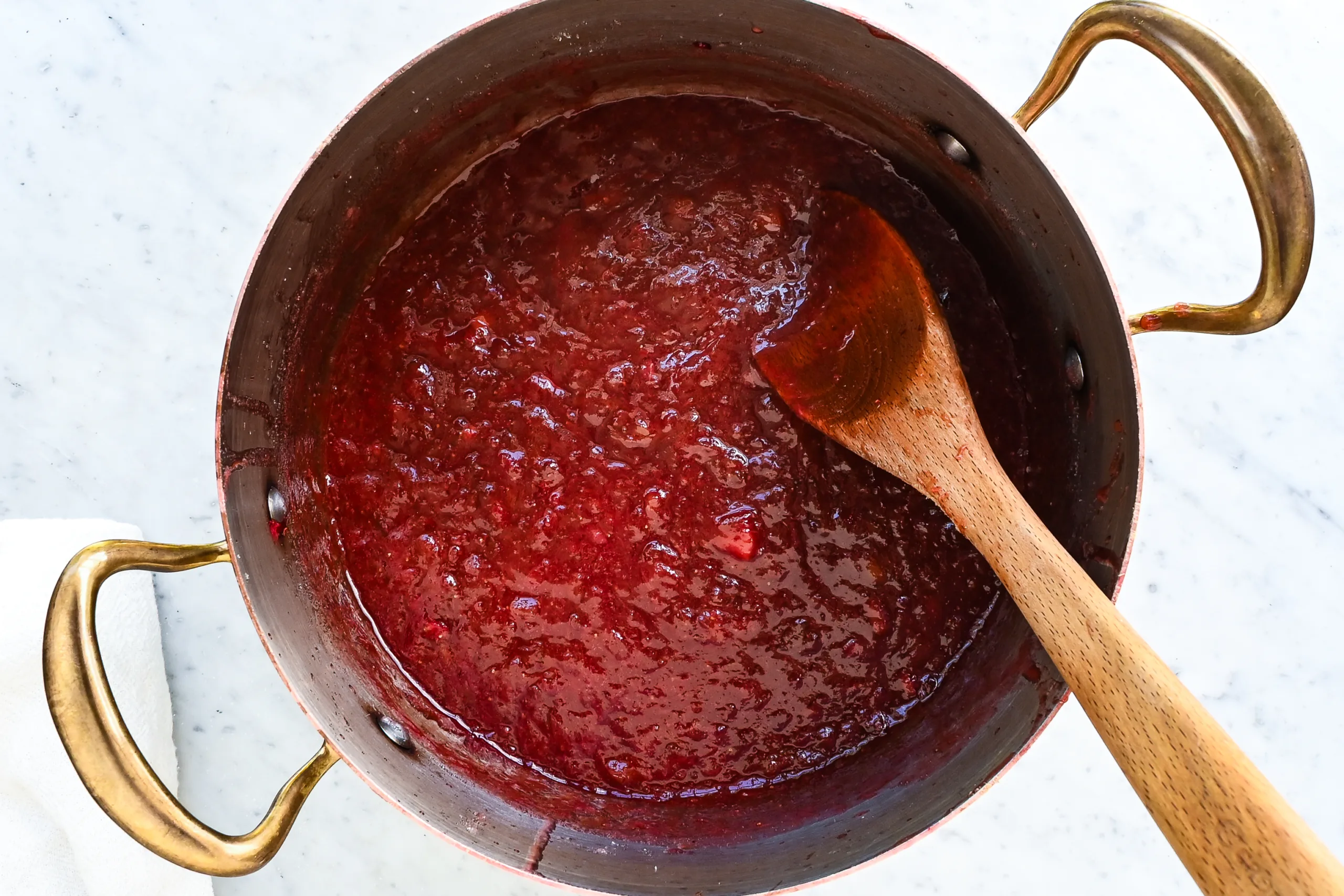 Thick strawberry rhubarb jam cooked down in a pot with a wooden spoon.