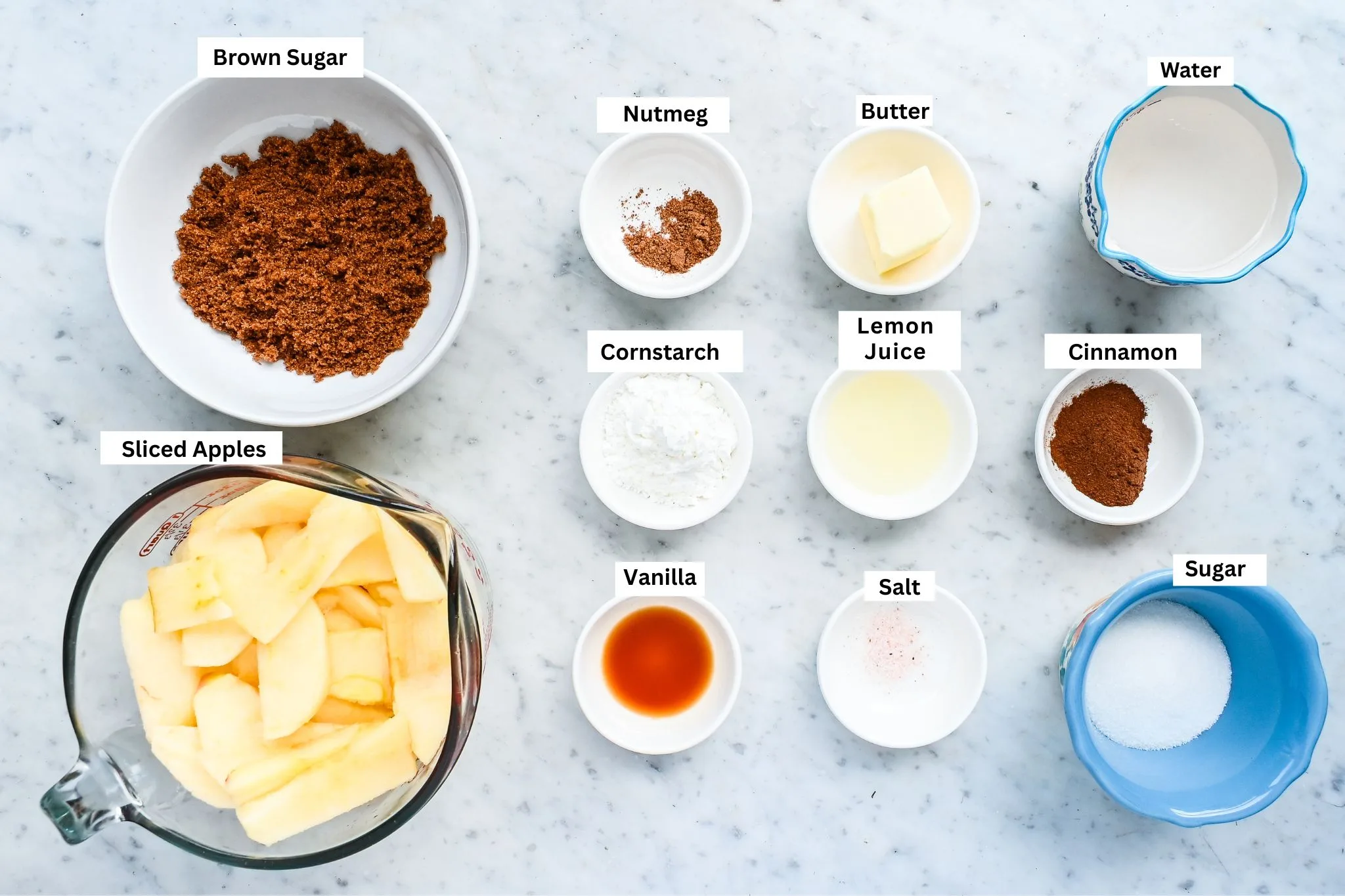 Ingredients for homemade apple pie filling arranged on a marble counter.