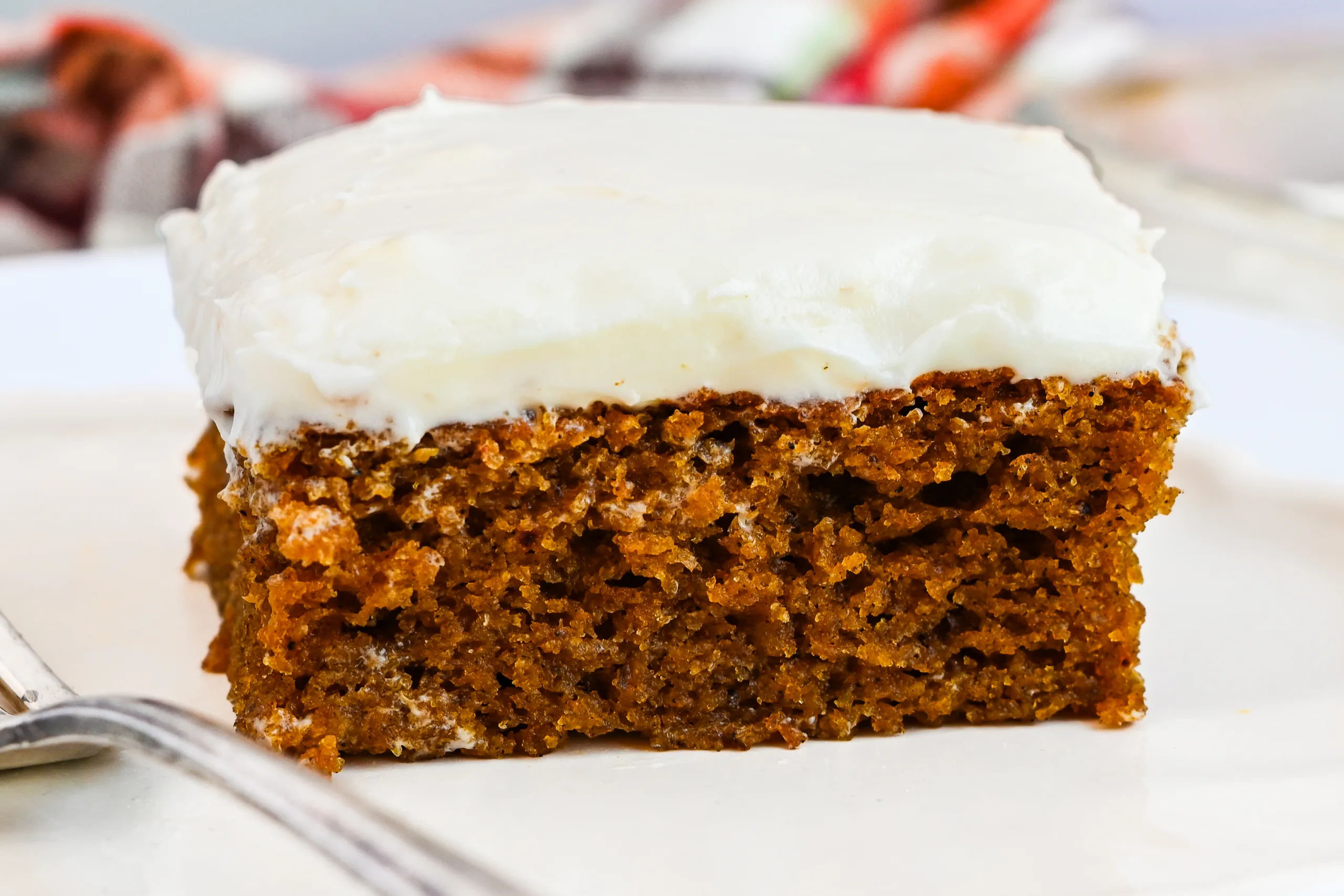 Pumpkin bar topped with cream cheese frosting on a white plate with a fork nearby.