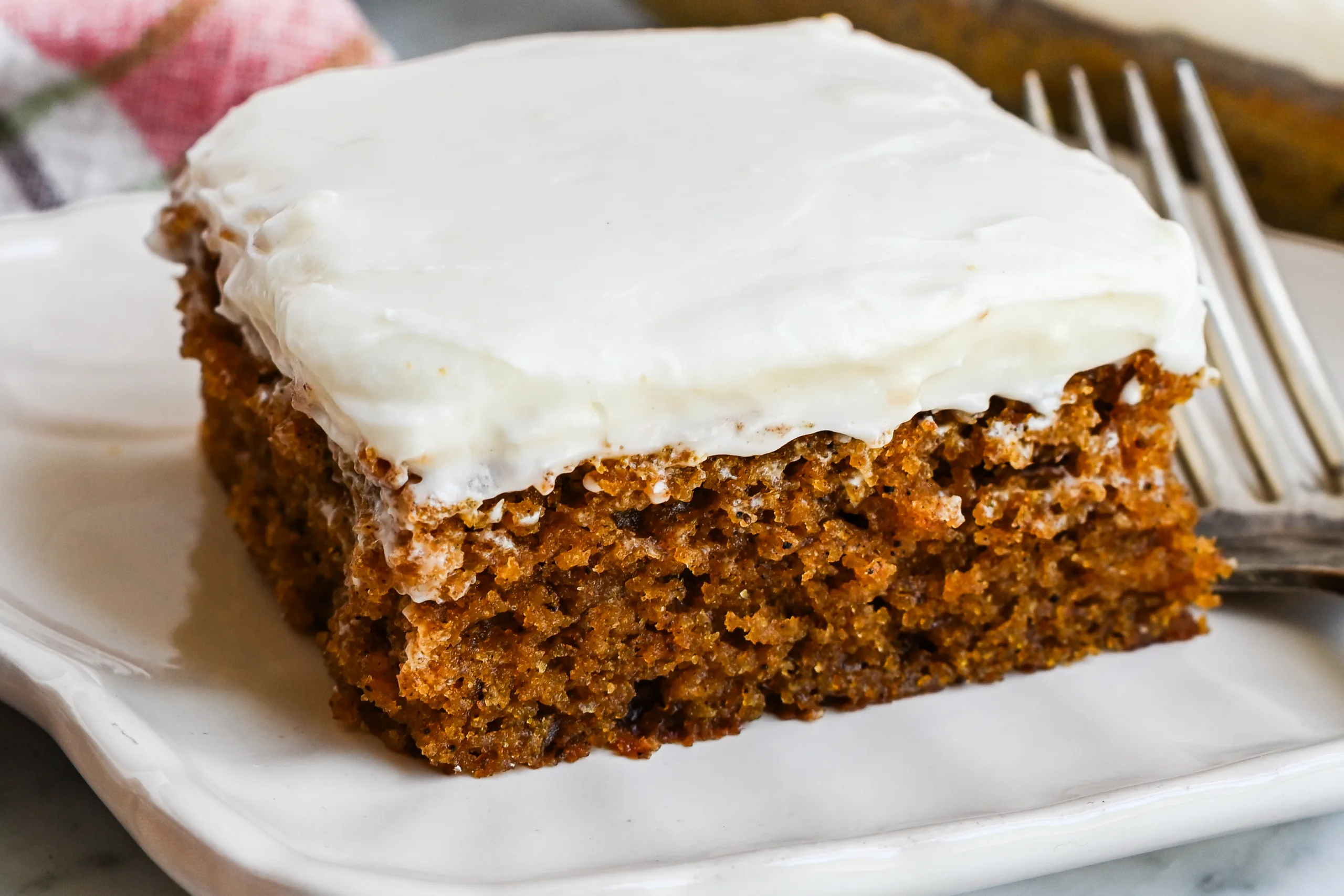 Pumpkin bar with thick cream cheese frosting served on a white plate with more bars in the background.