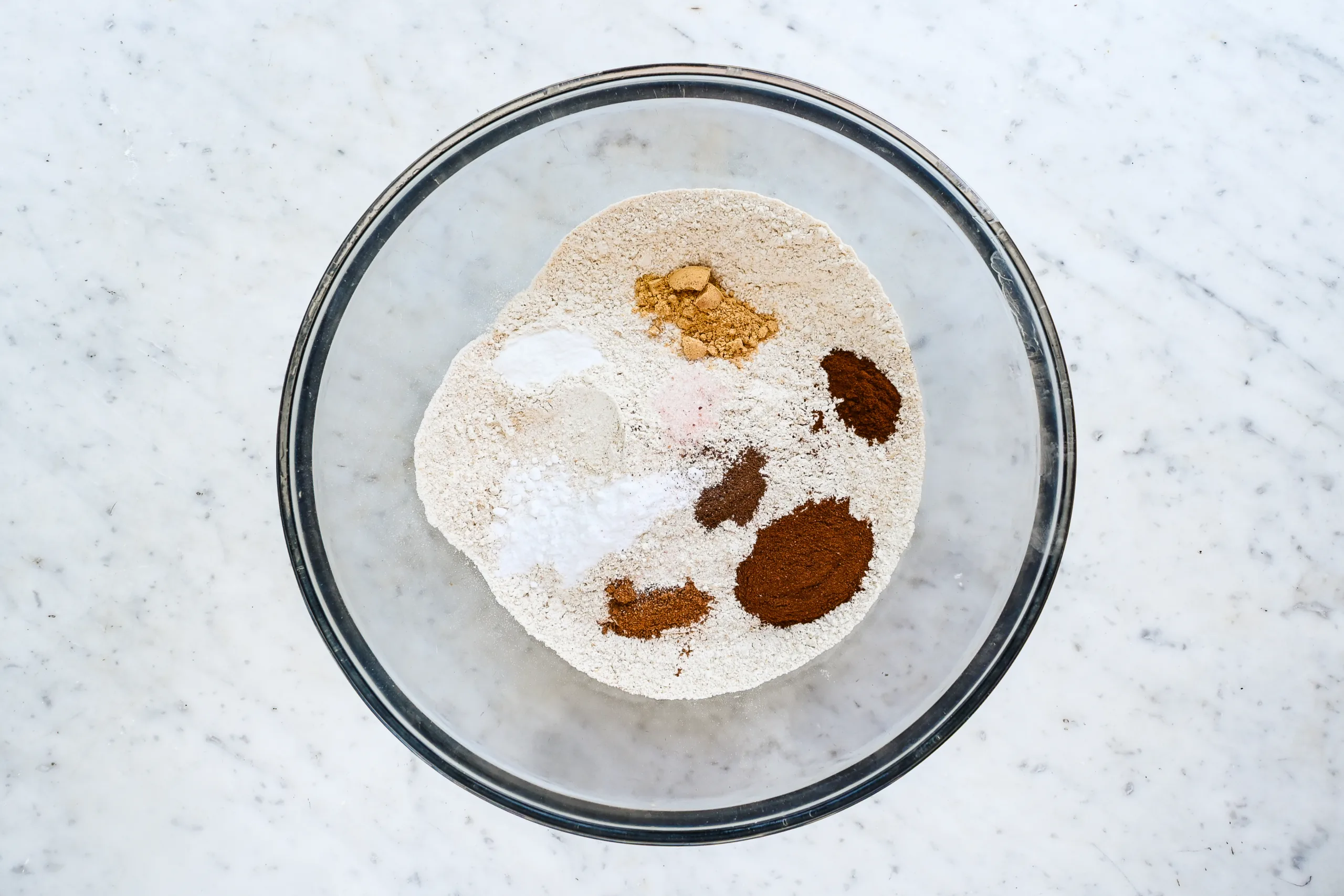 Flour, baking powder, baking soda, salt, and warm spices in a glass mixing bowl.