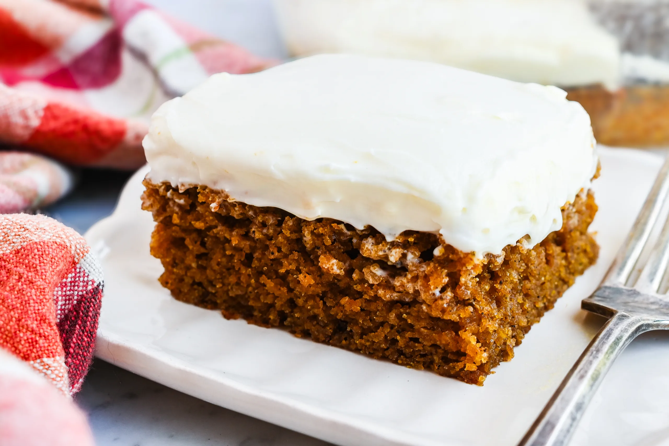 Tight close-up of a pumpkin bar topped with cream cheese frosting, showing the moist pumpkin crumb and smooth frosting layer.