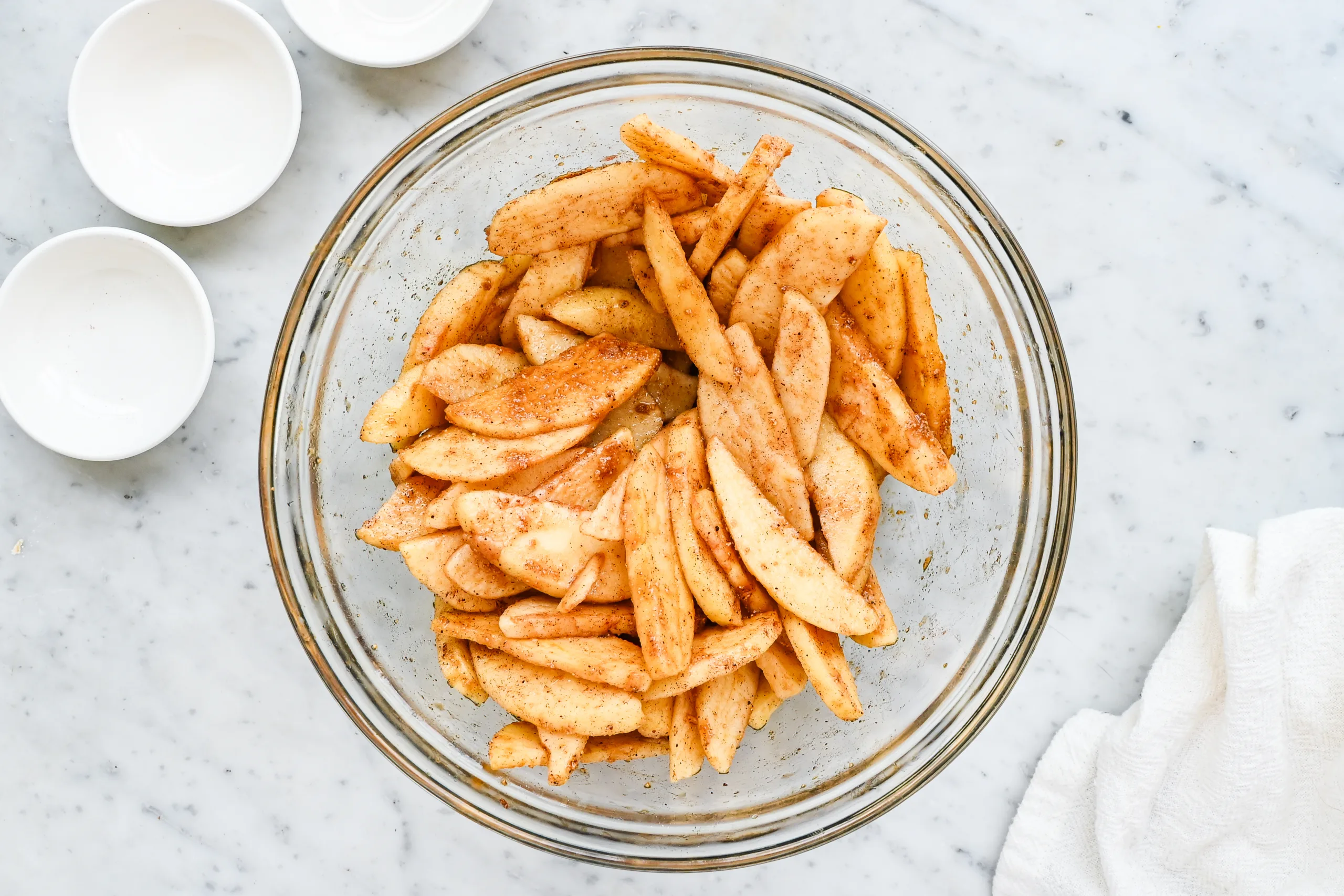 Apple slices coated with cinnamon sugar mixture in a glass mixing bowl.