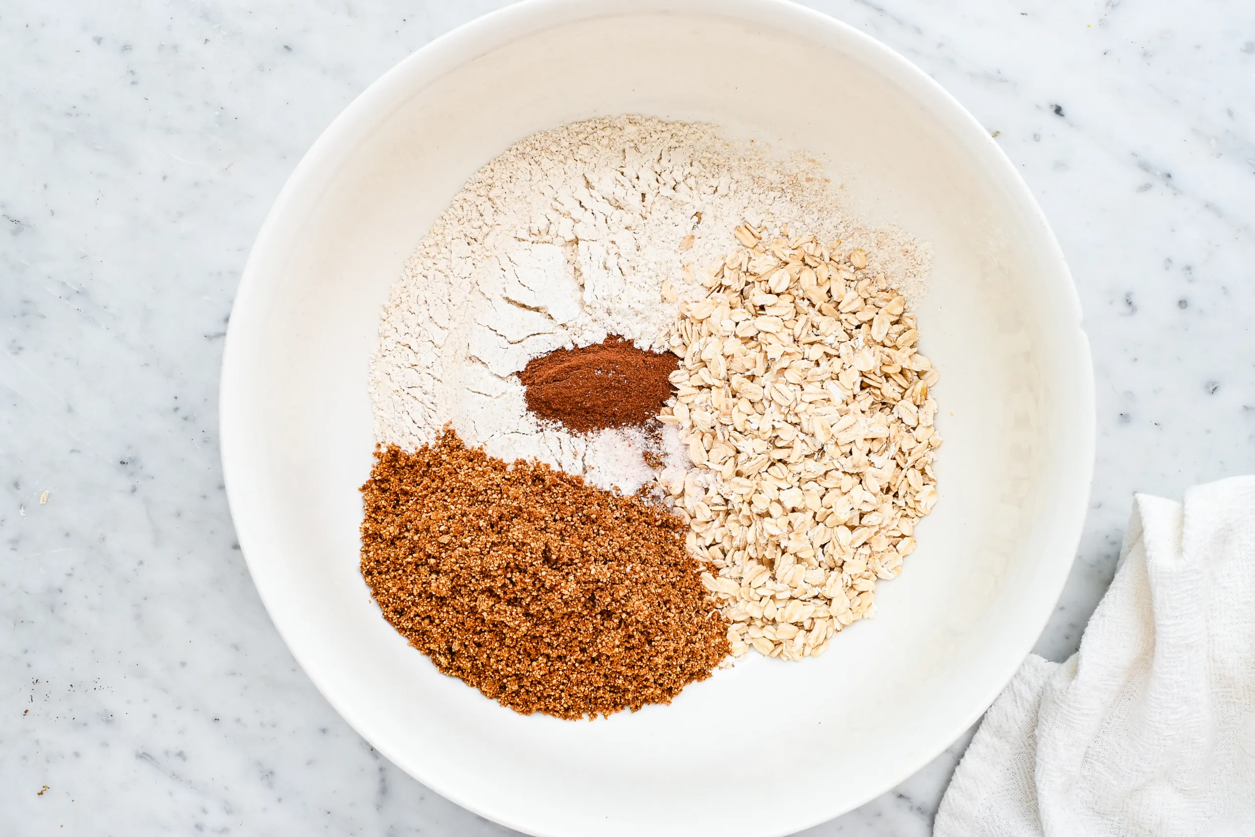 Flour, oats, brown sugar, cinnamon, and salt in a white mixing bowl for the oat crumble topping.