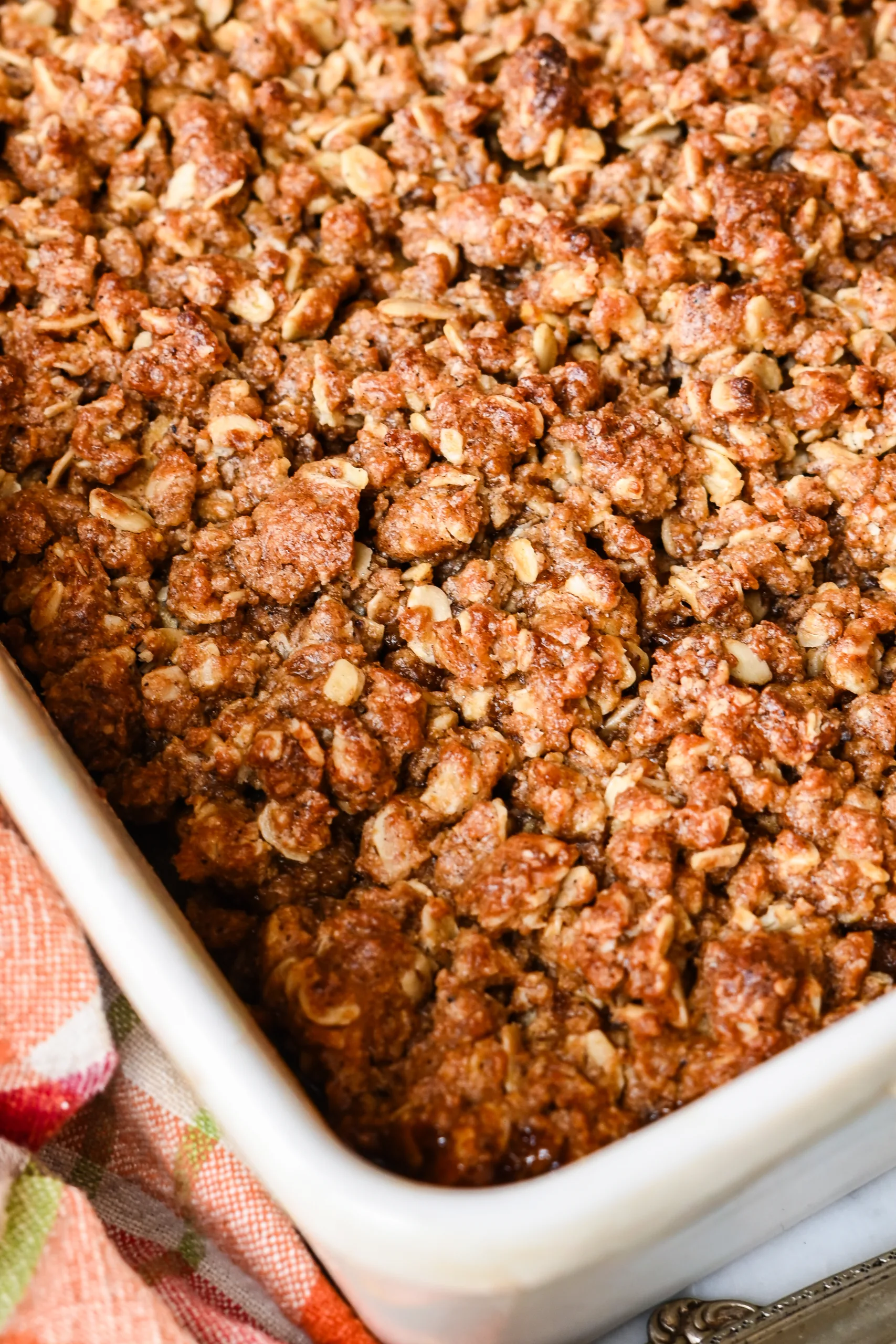 Close-up of golden oat crumble topping on baked apple crisp in a white baking dish.