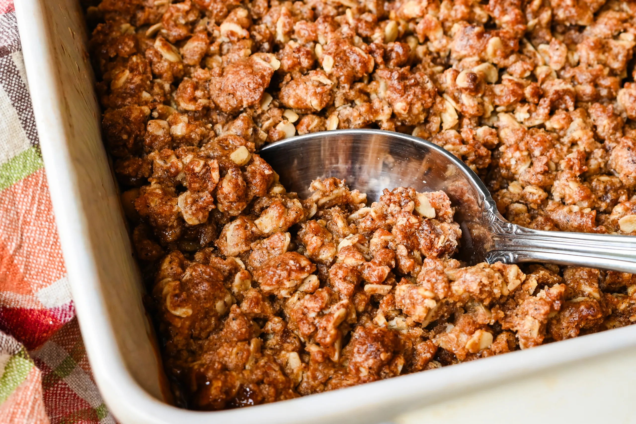 Spoon serving sourdough apple crisp from a baking dish with crisp oat crumble topping.