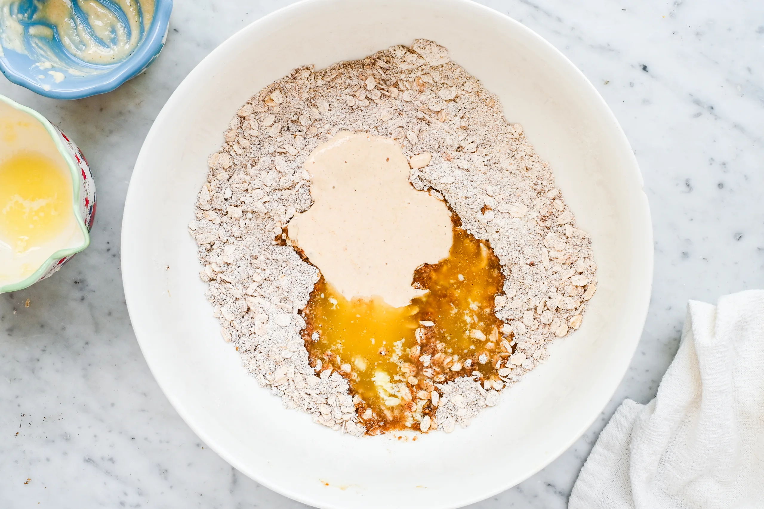 Sourdough oat crumble topping mixed in a white bowl with a wooden spoon.