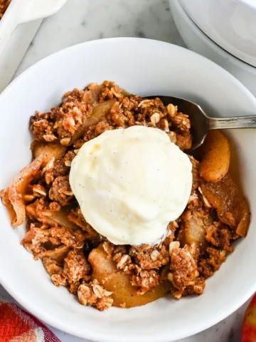 Easy homemade sourdough apple crisp with oat crumble topping served warm in a white bowl with vanilla ice cream and fresh apples nearby.