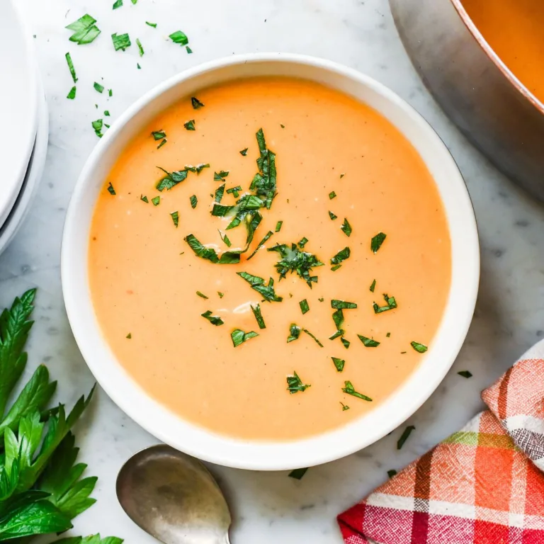Creamy butternut pumpkin sweet potato soup in a white bowl with parsley, a copper pot, plates, and a plaid towel nearby.