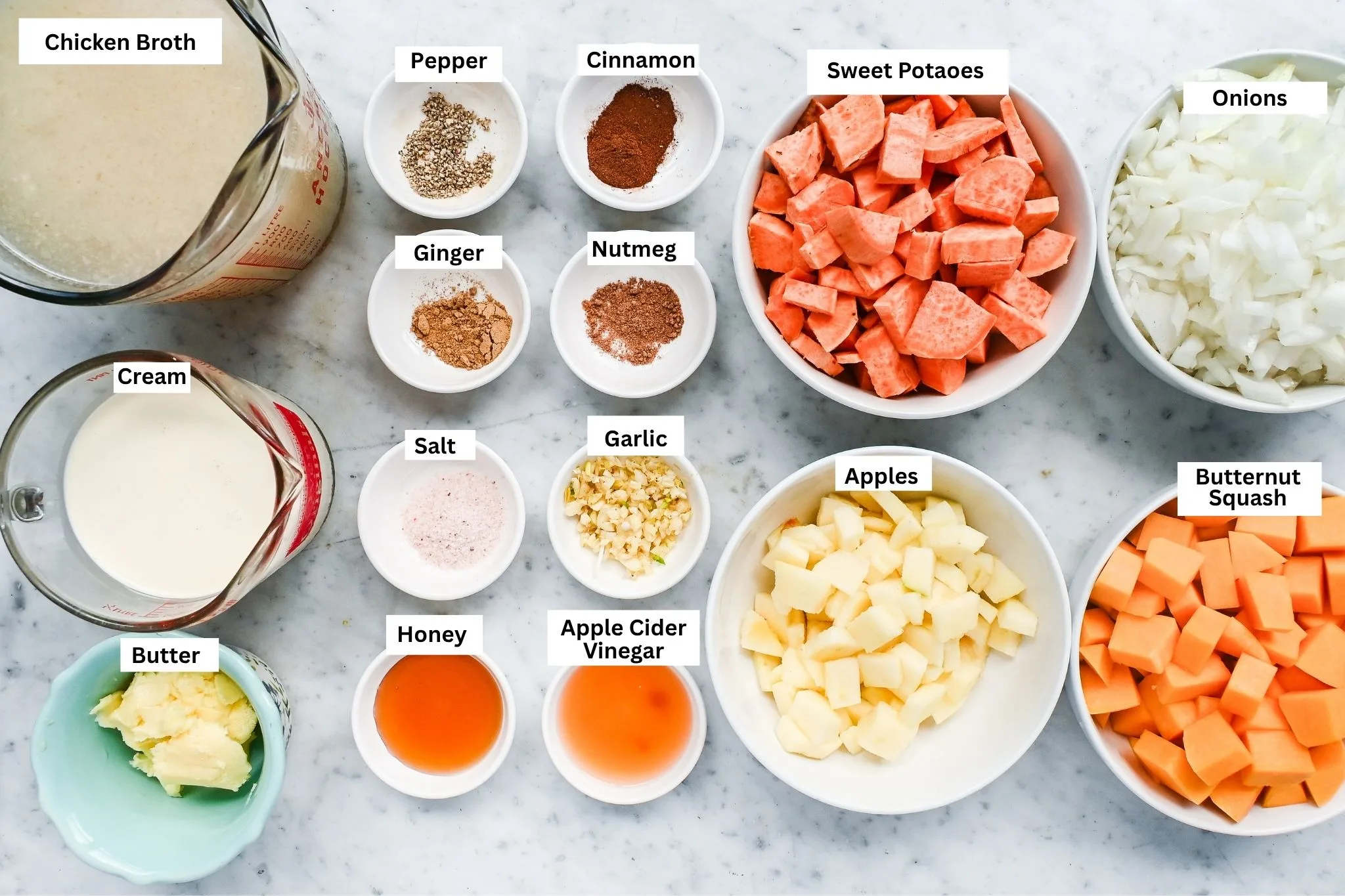 Butternut pumpkin sweet potato soup ingredients arranged on a marble counter with squash, sweet potatoes, apple, onion, broth, cream, butter, honey, garlic, and spices.