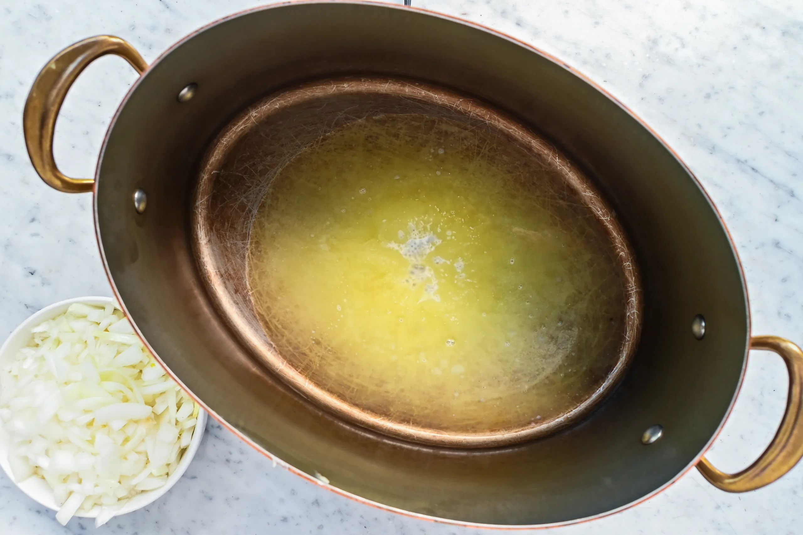 Butter melting in a copper pot with chopped onions nearby.