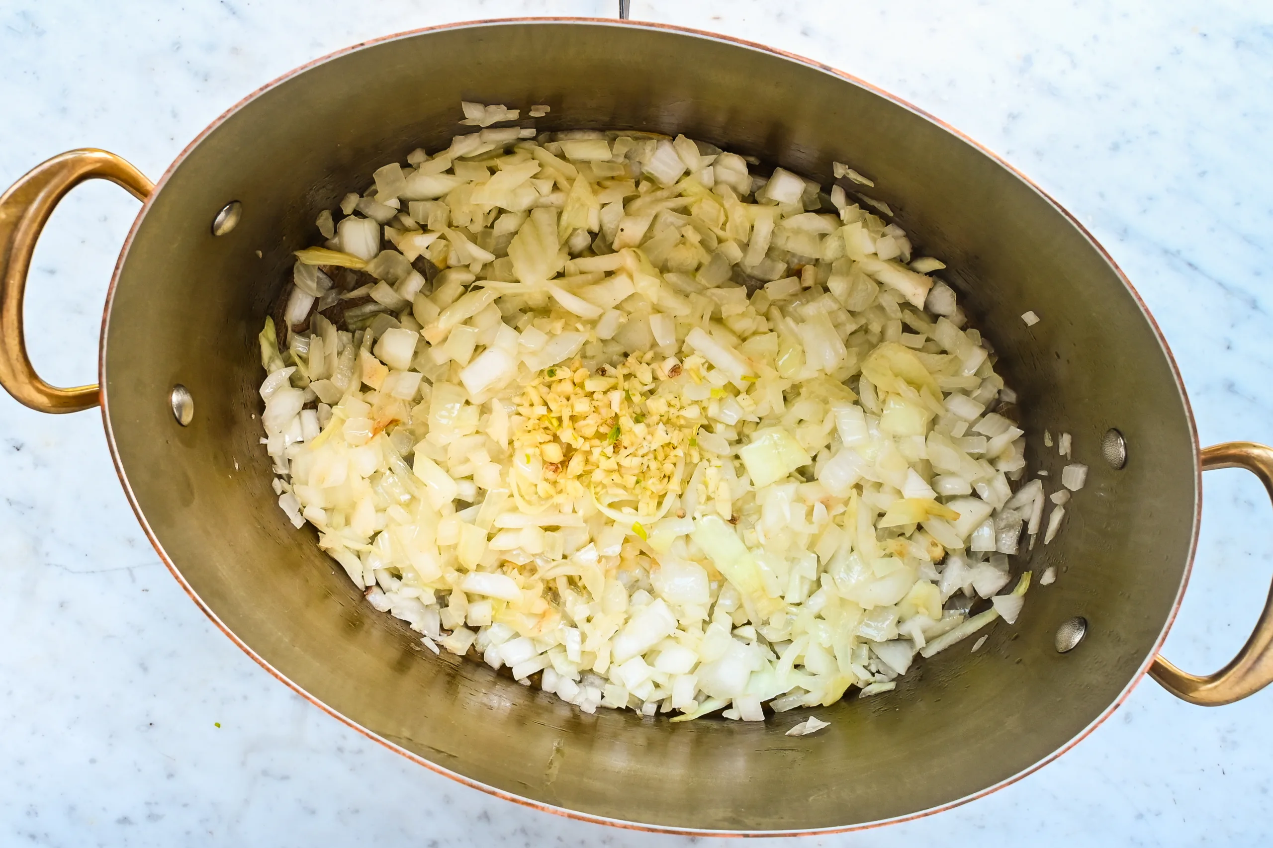 Sautéed onions and minced garlic in a copper pot.