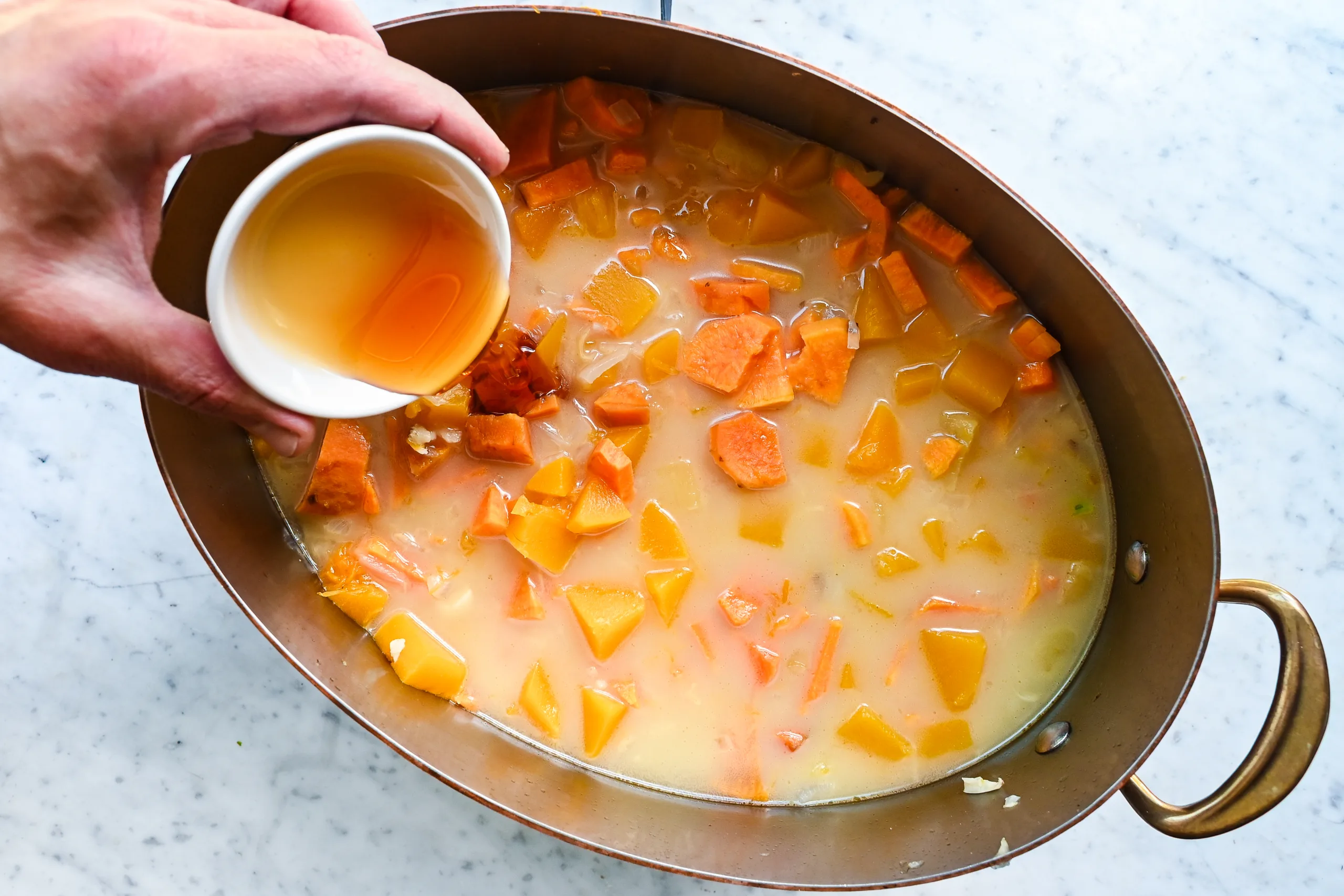 Honey being poured into butternut pumpkin sweet potato soup as the vegetables simmer.