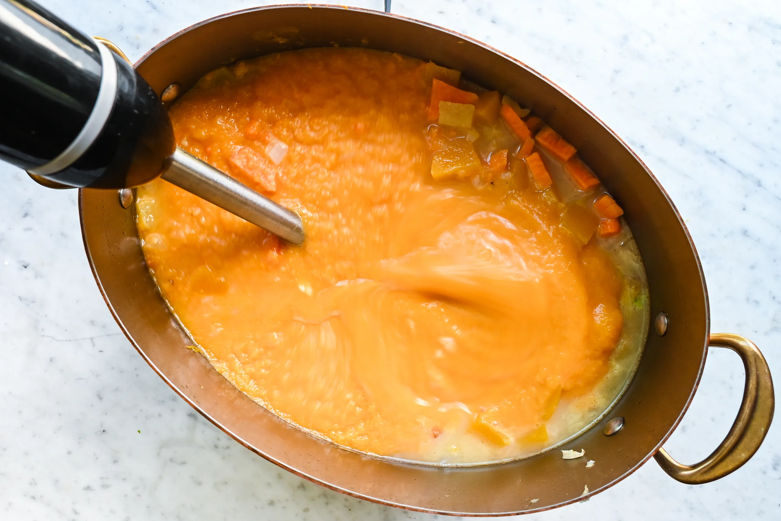 Butternut pumpkin sweet potato soup being blended with an immersion blender.