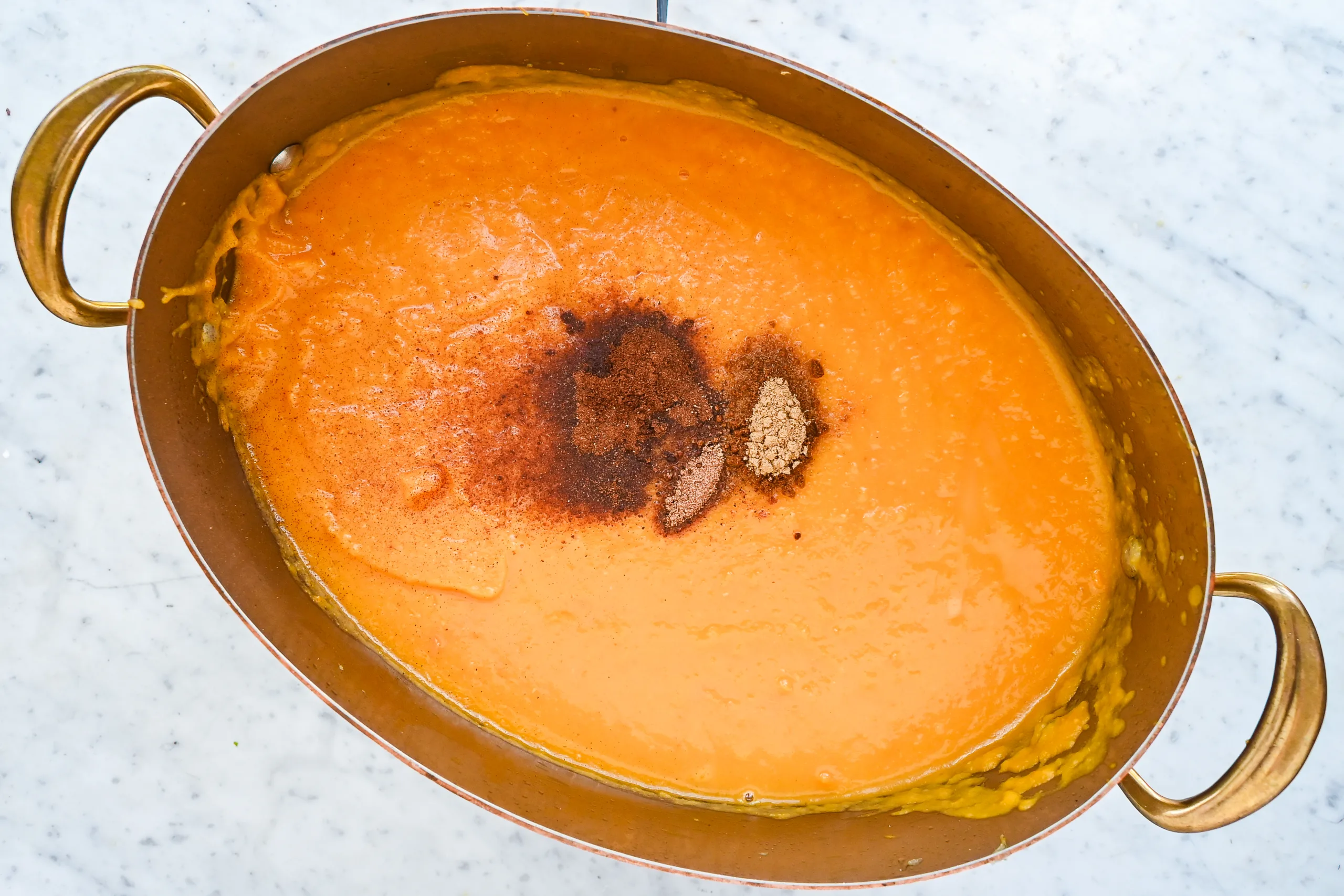 Warm spices added to blended butternut pumpkin sweet potato soup in a copper pot.