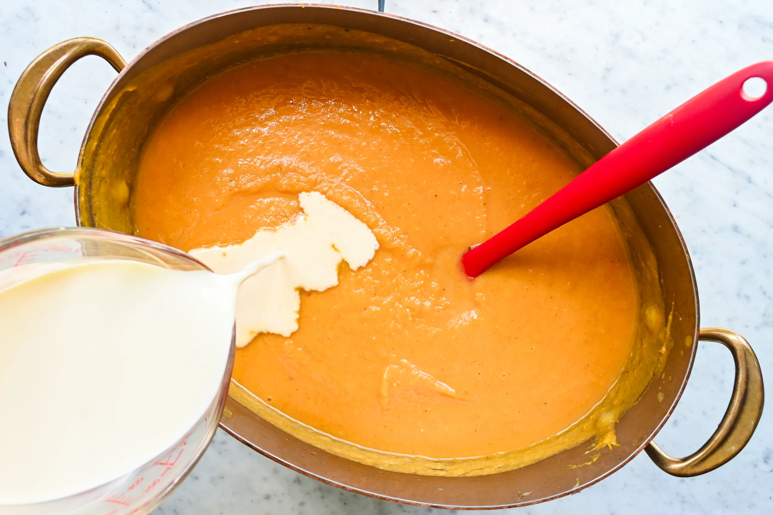 Heavy cream being poured into blended butternut pumpkin sweet potato soup.