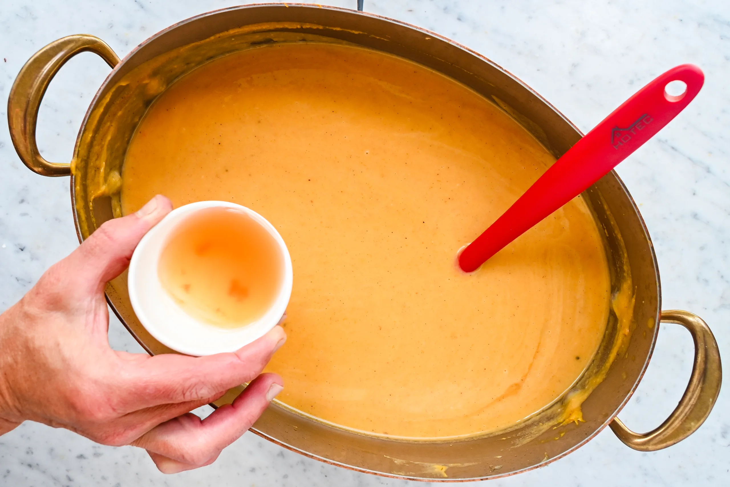 A small bowl of apple cider vinegar being added to creamy butternut pumpkin sweet potato soup.