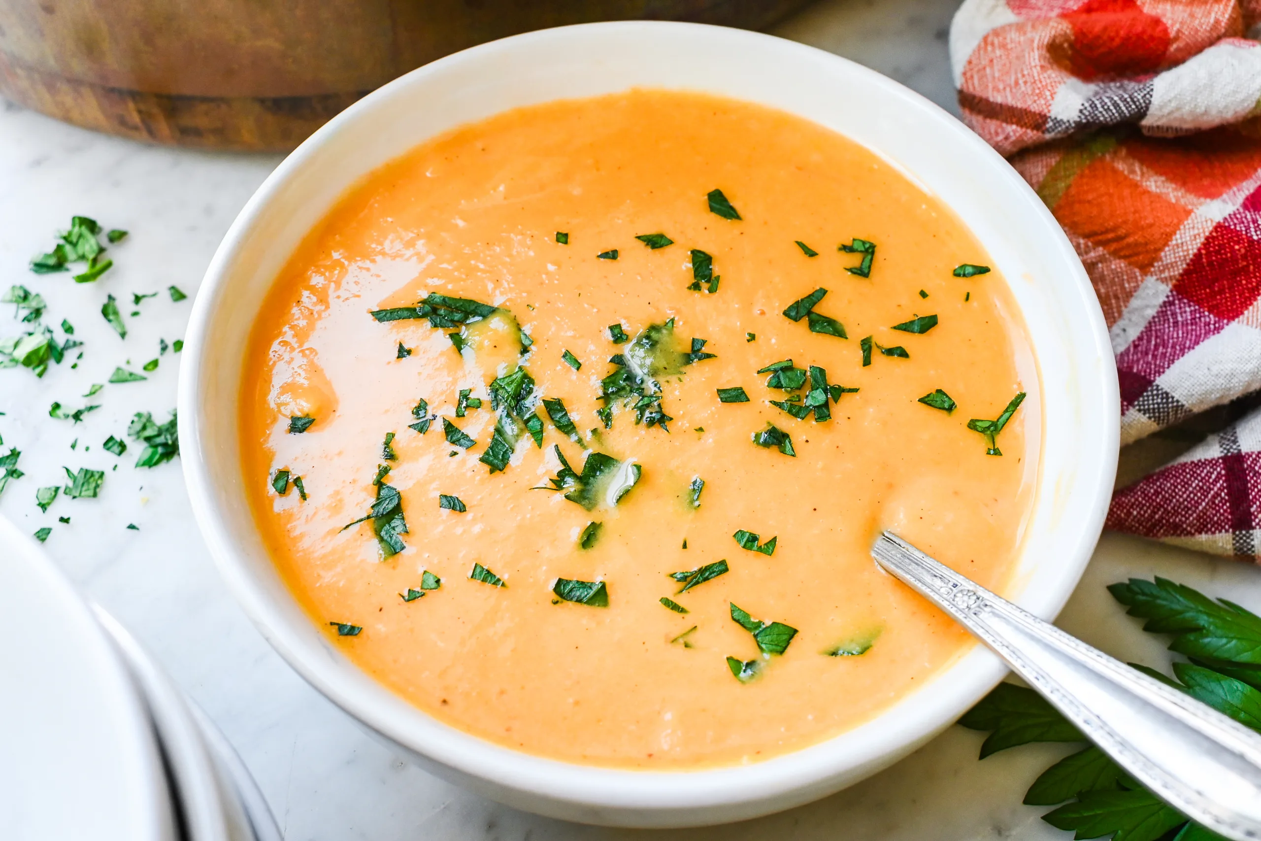 Creamy butternut pumpkin sweet potato soup served in a bowl with parsley and a spoon.