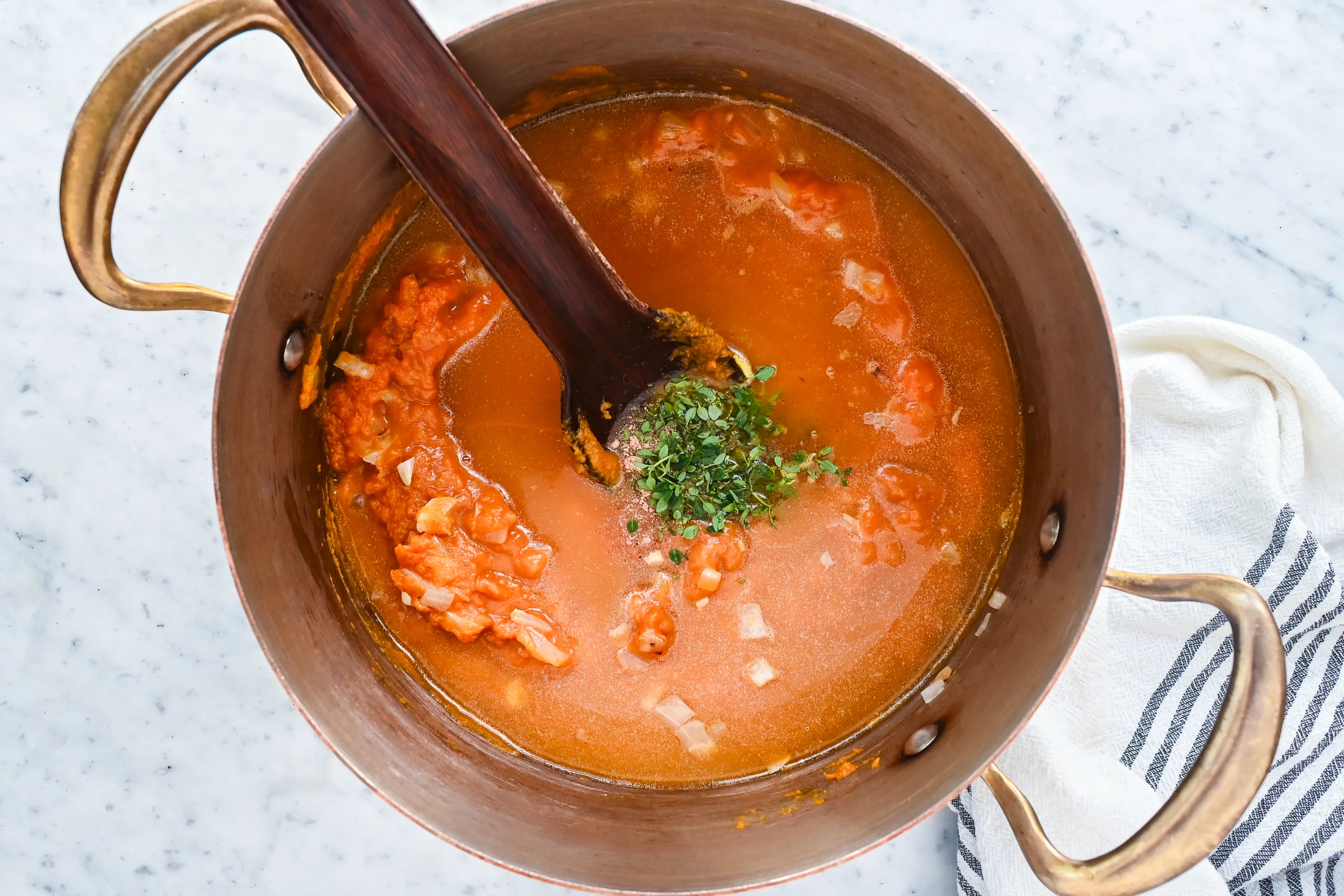 Broth, thyme, and seasonings added to pumpkin purée in a copper pot.