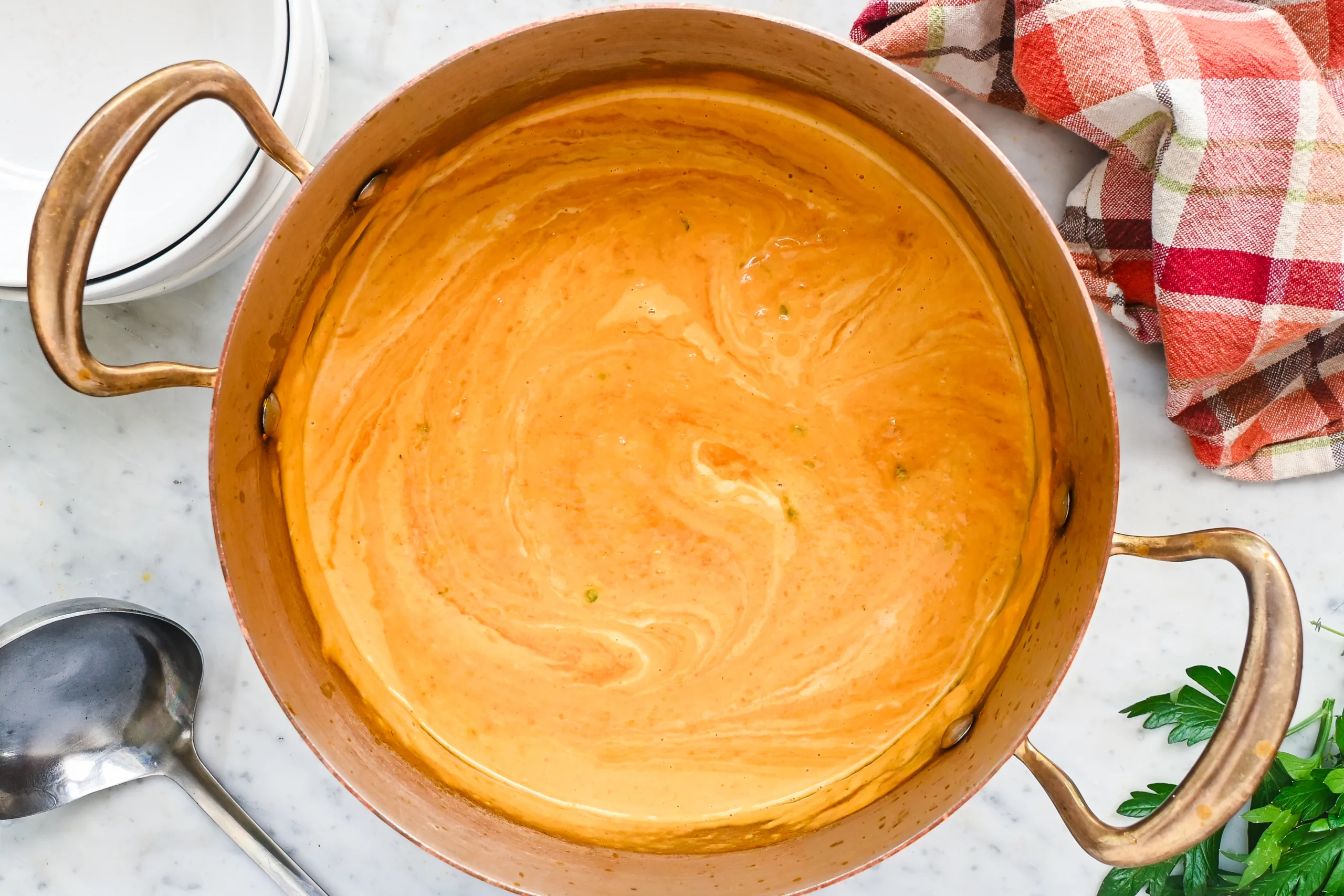 Creamy pumpkin soup in a copper pot with swirls of cream.
