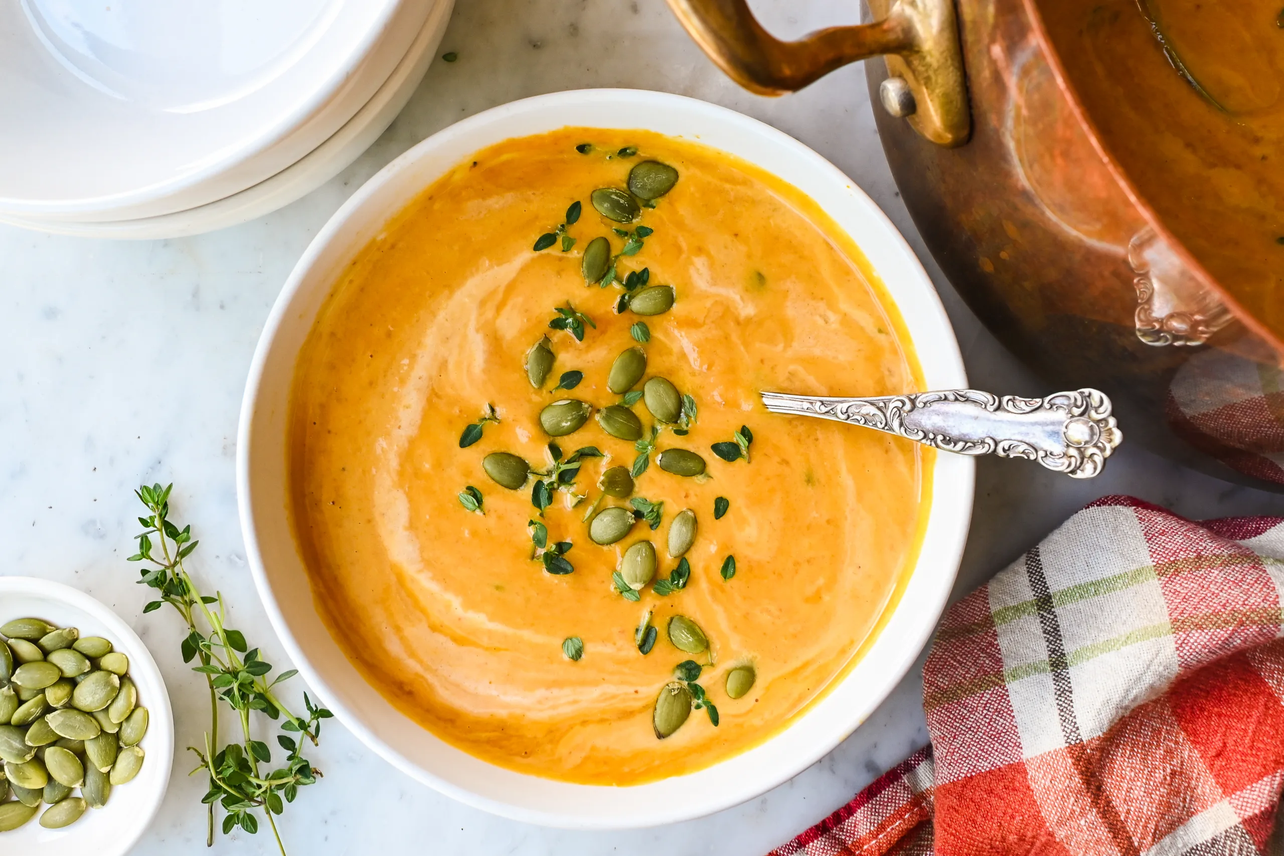 Creamy pumpkin soup served in a bowl with pumpkin seeds, thyme, and a spoon.