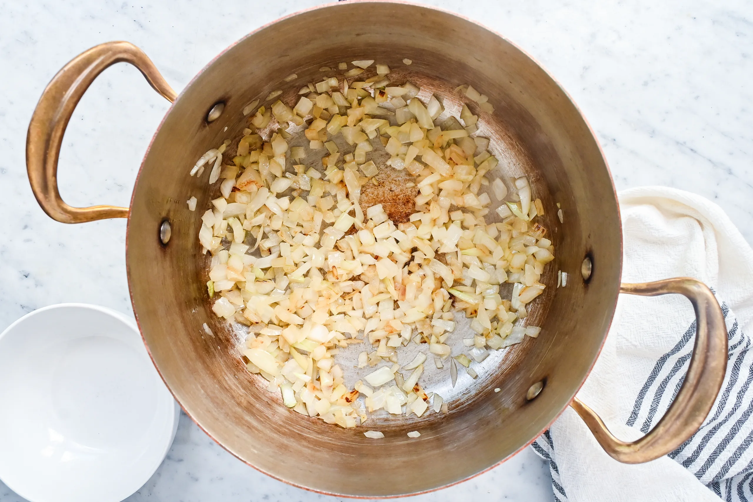 Chopped onions cooking in a copper pot.